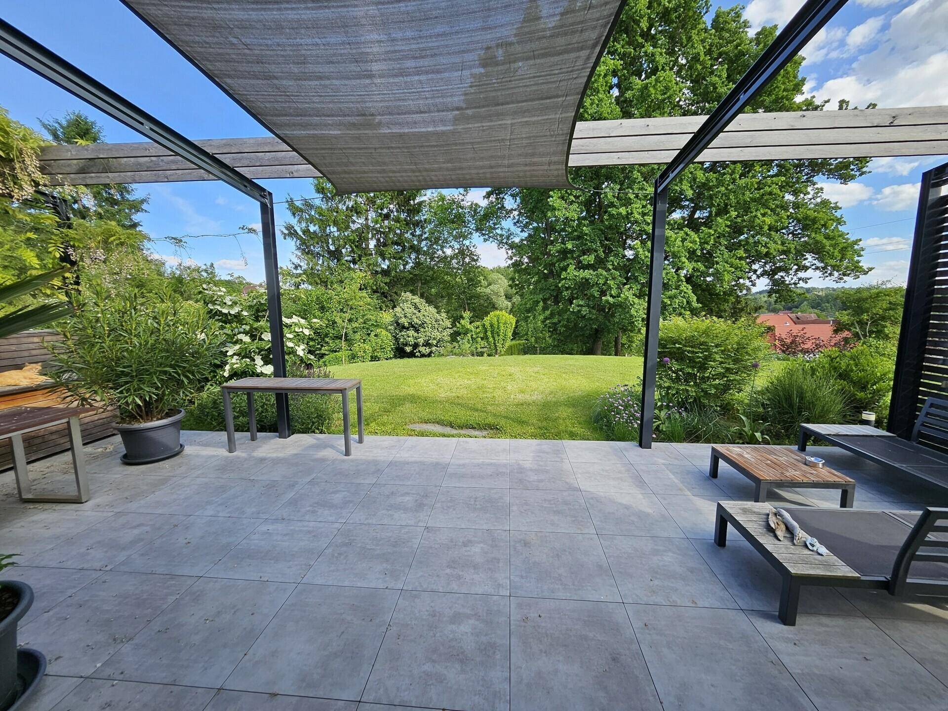 Großzügige Terrasse mit Pergola, Fliesenboden und weitem Blick ins Grüne.