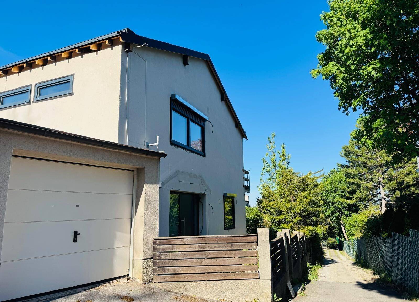 Seitenansicht des Hauses mit Garage und Zufahrt, umgeben von Bäumen und Hecken.