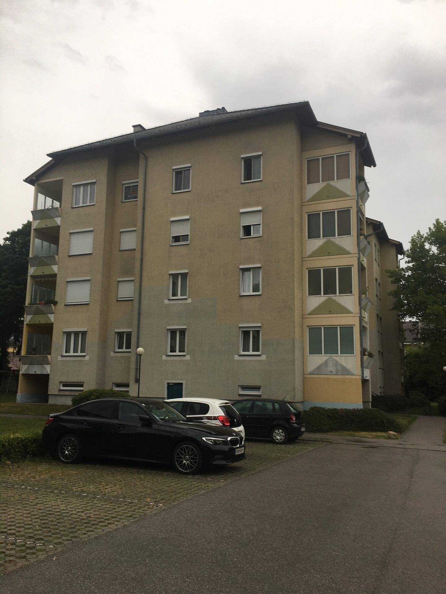 Mehrstöckiges Wohngebäude mit mehreren Balkonen und parkenden Autos davor.