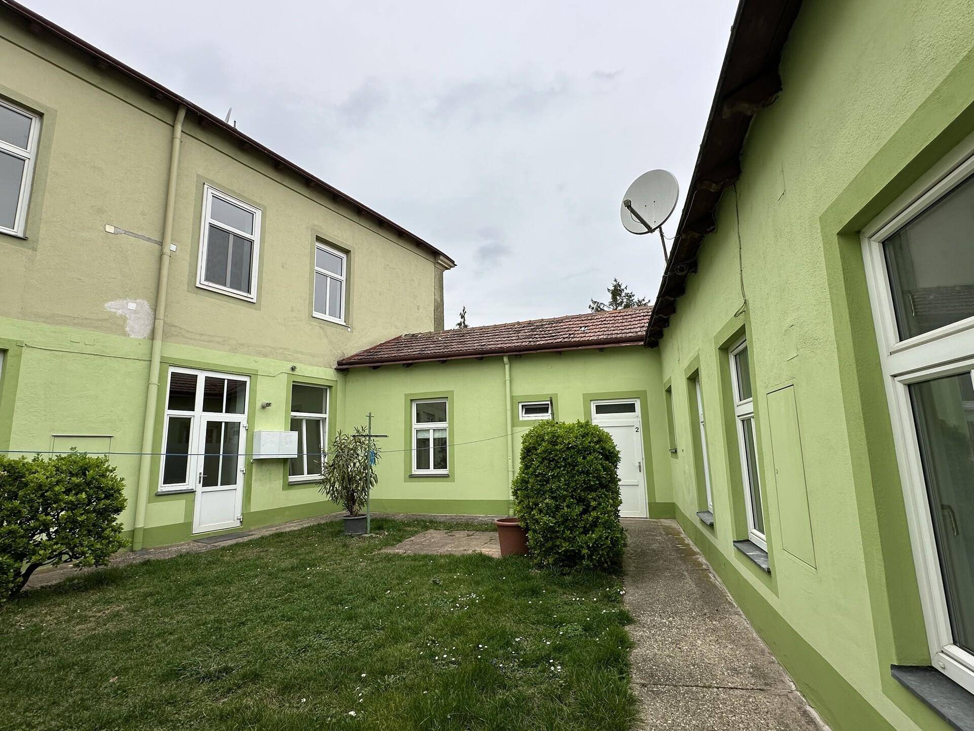 Hinterhof mit Rasenfläche und einem Satellitenempfänger an der Gebäudewand.