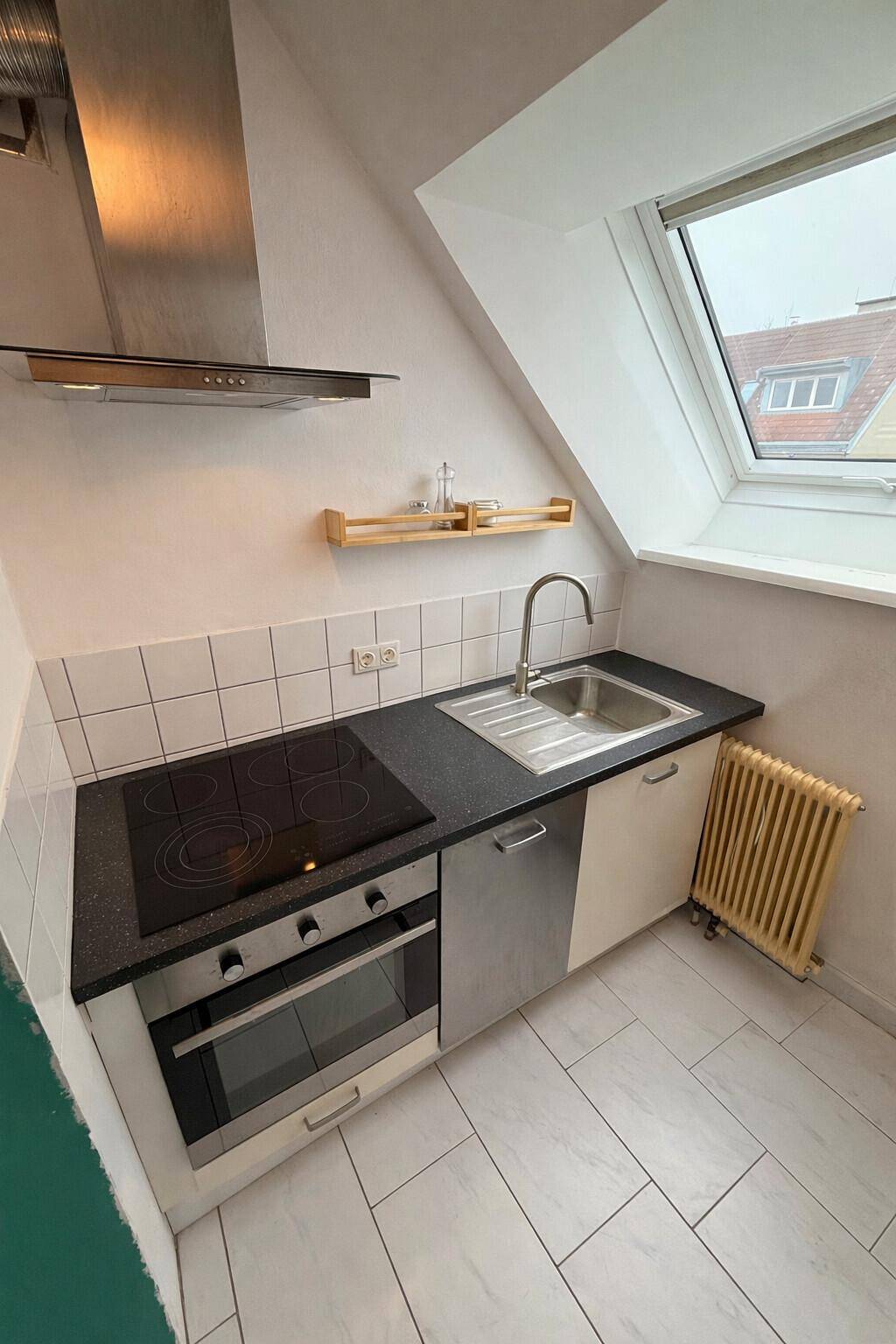 Funktionale Küche mit Induktionskochfeld, Backofen und Spüle unter dem Dachfenster.