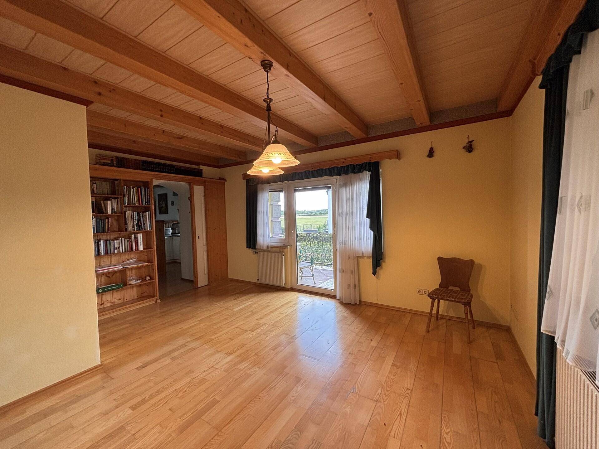 Geräumiges Wohnzimmer mit Holzbalkendecke, Parkettboden und Zugang zu einem Balkon mit Weitblick.