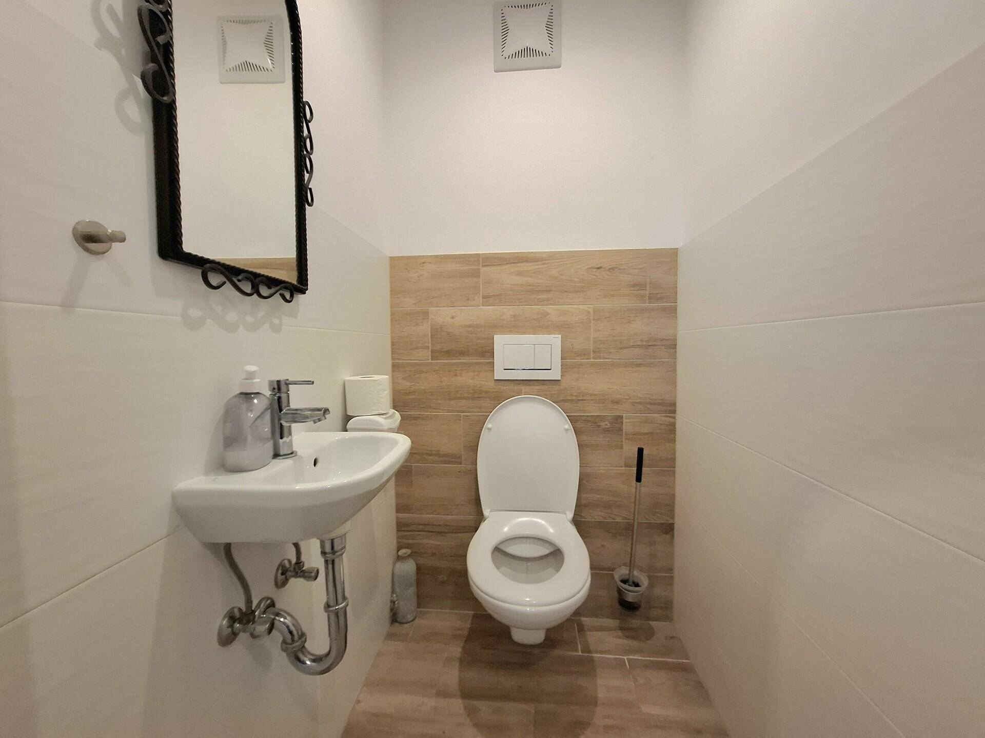 Modernes Gäste-WC mit Wand-WC, kleinem Waschbecken und hellen Fliesen.