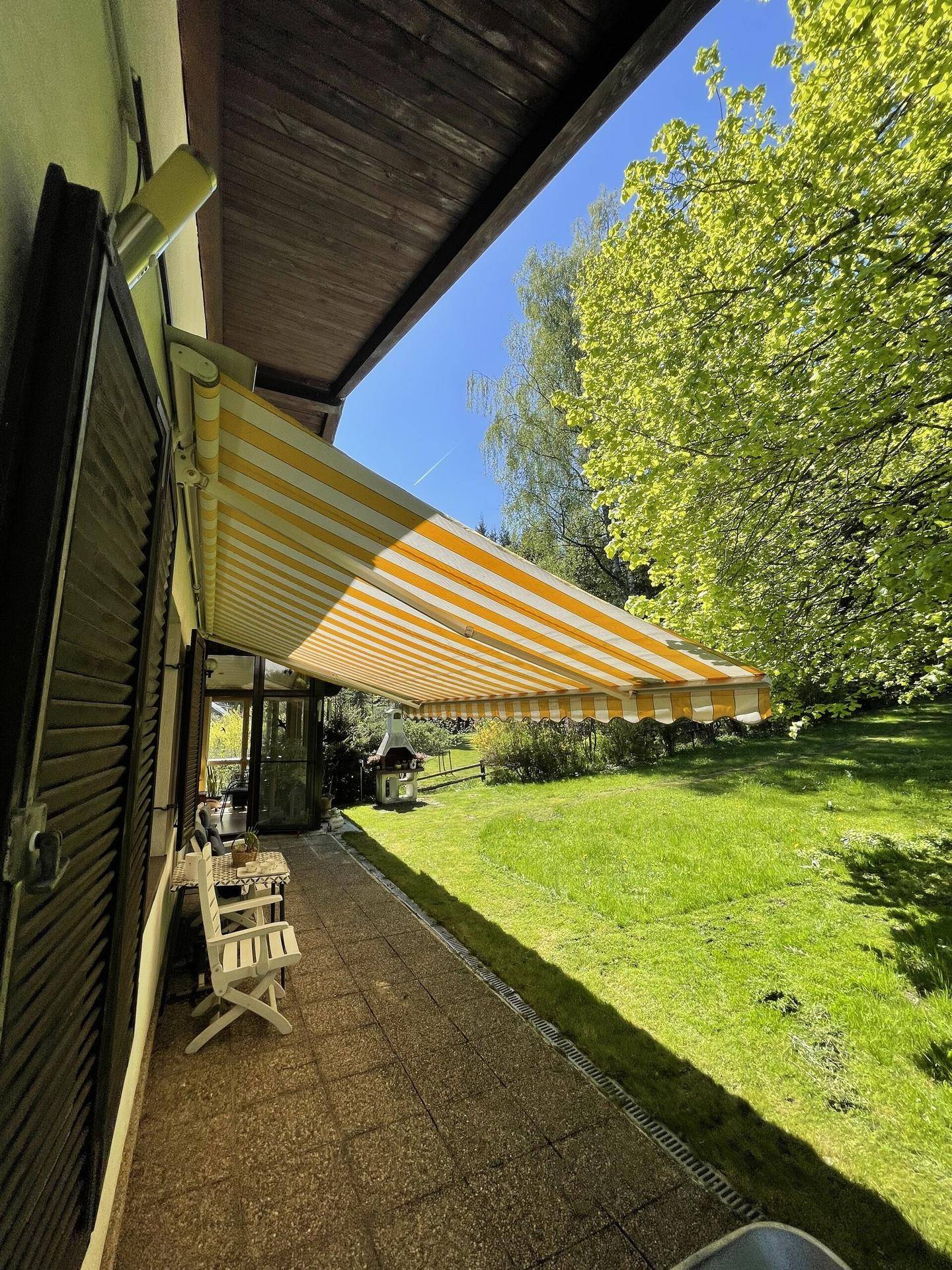 Gedeckte Terrasse mit gestreifter Markise und Blick auf den grünen Garten.