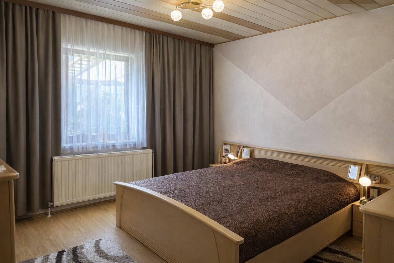 Gemütliches Schlafzimmer mit Holzbalkendecke, Doppelbett und Fenster mit Vorhängen.