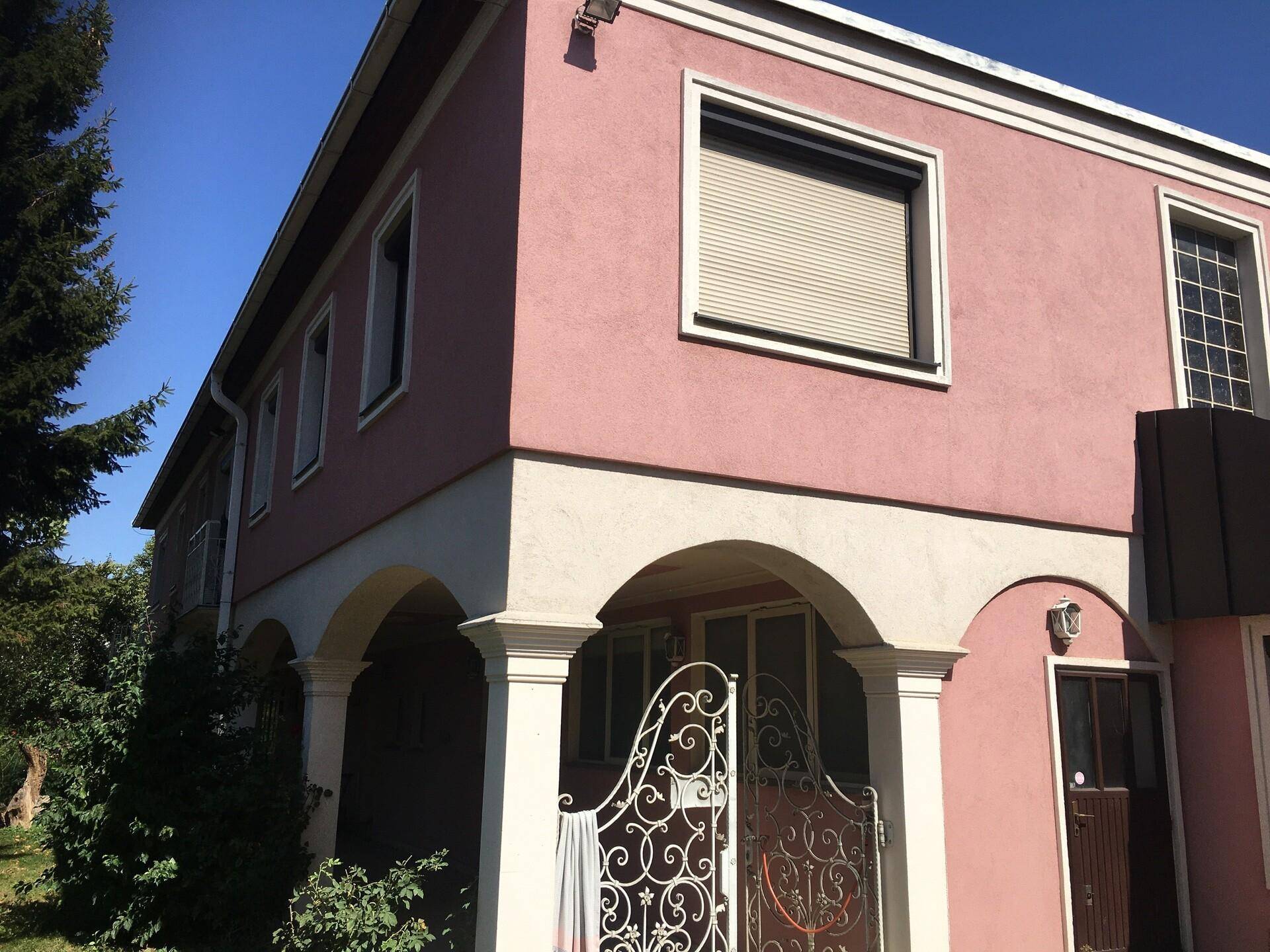 Fassade eines Hauses in Rosa mit weißen Bögen und einem dekorativen Tor.
