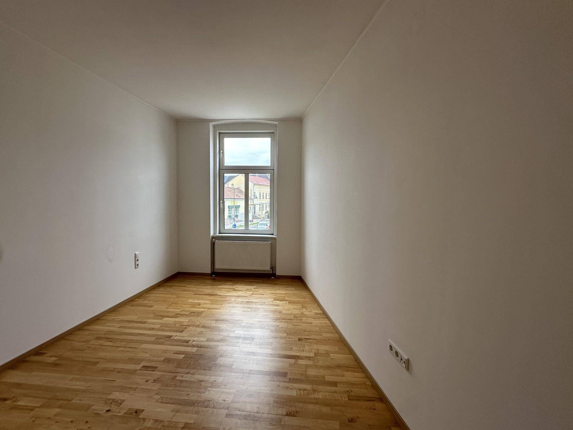 Helles Schlafzimmer mit Parkettboden und einem Fenster, bietet viel Potenzial für persönliche Gestaltung.