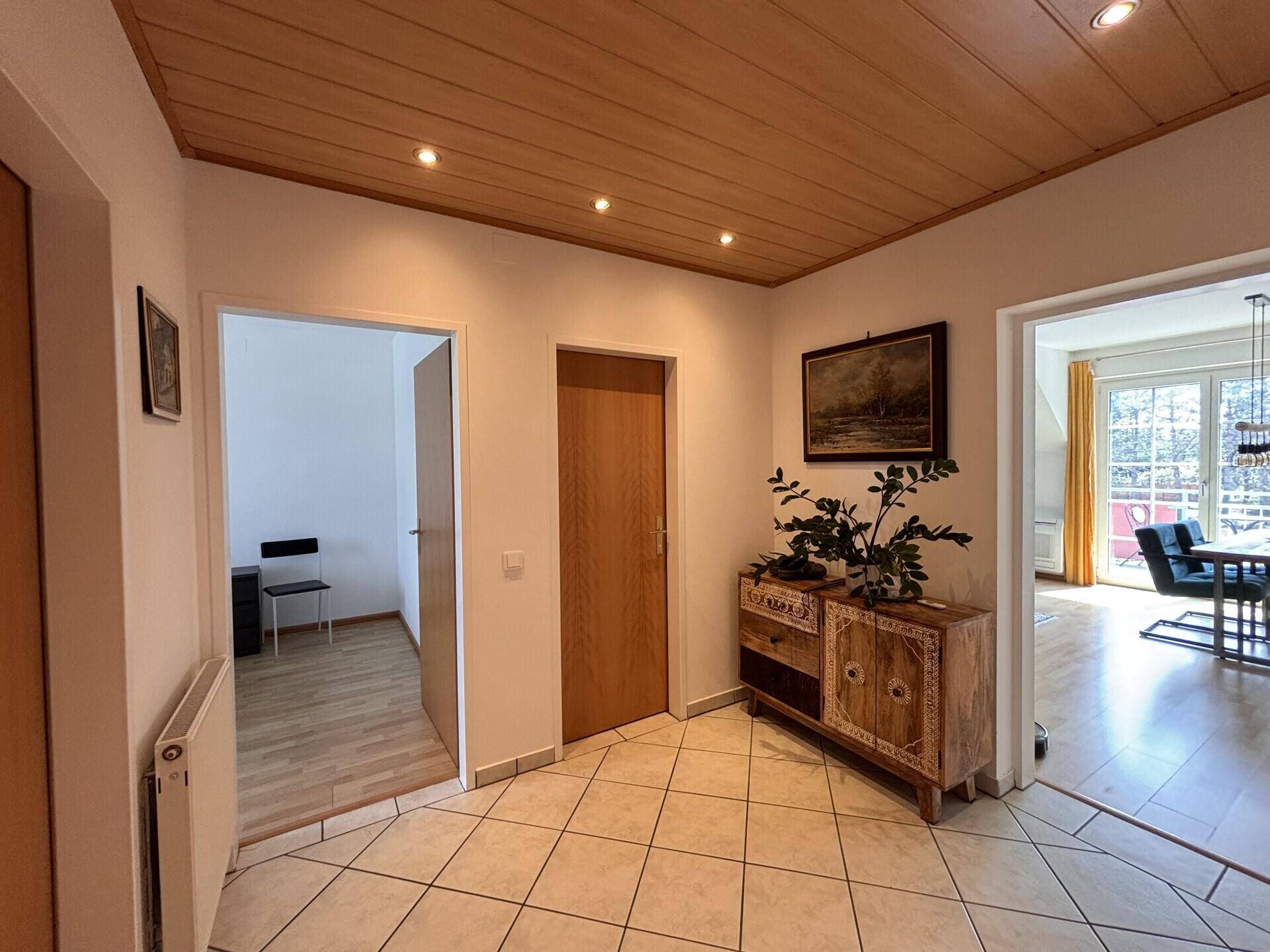 Flur mit Fliesenboden, Holzdecke und einem dekorativen Holzschrank.