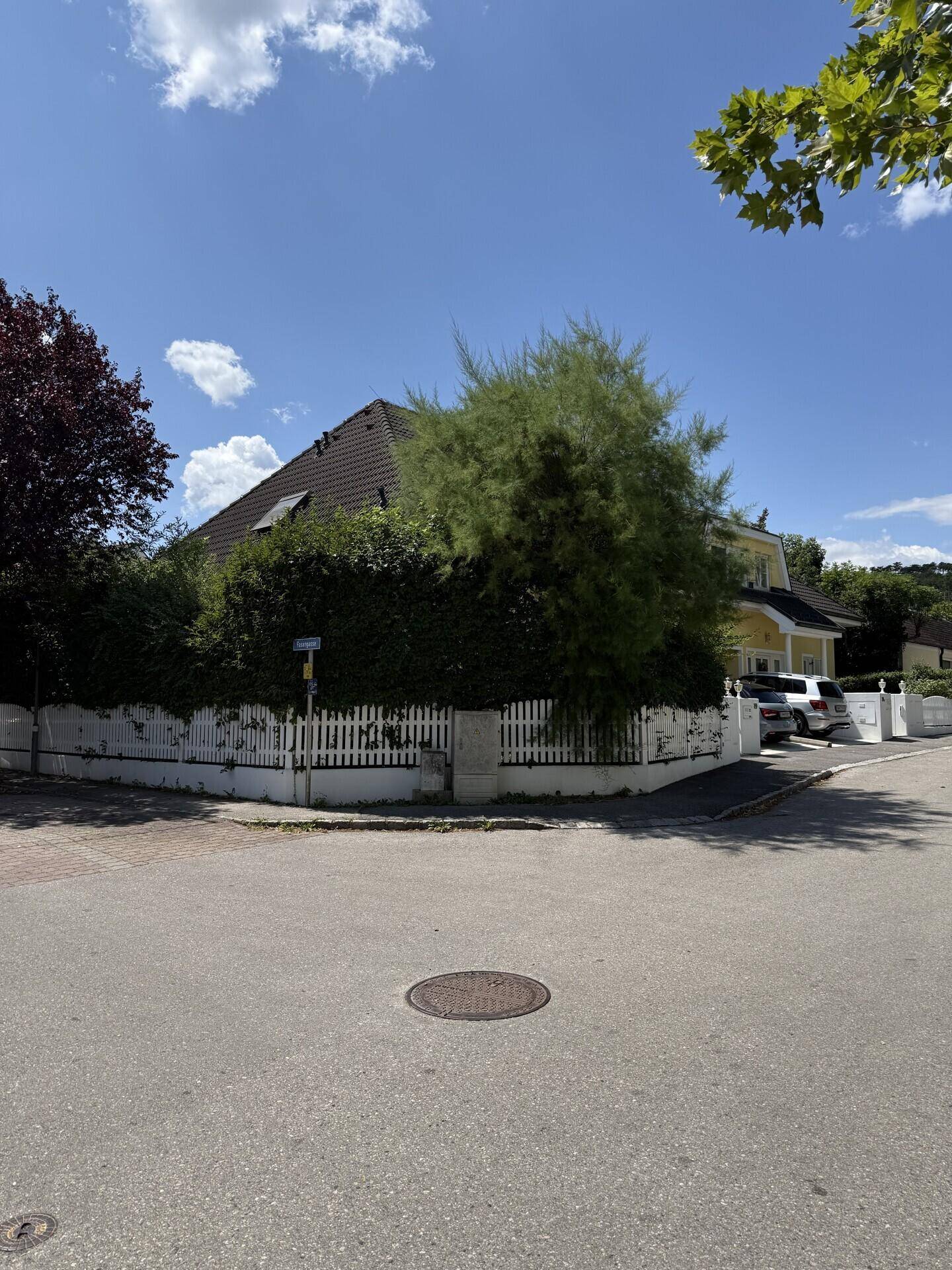 Ansicht des Hauses von der Straße mit weißem Zaun und üppiger Bepflanzung.