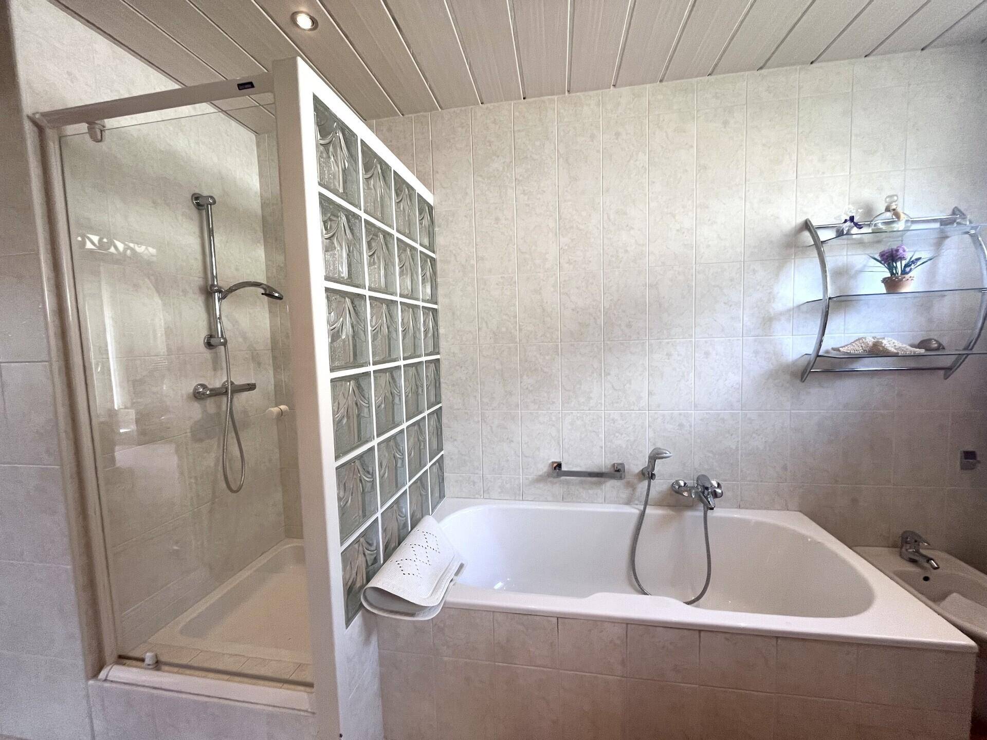 Badezimmer mit Badewanne, Duschkabine aus Glasbausteinen und Bidet, komplett gefliest.