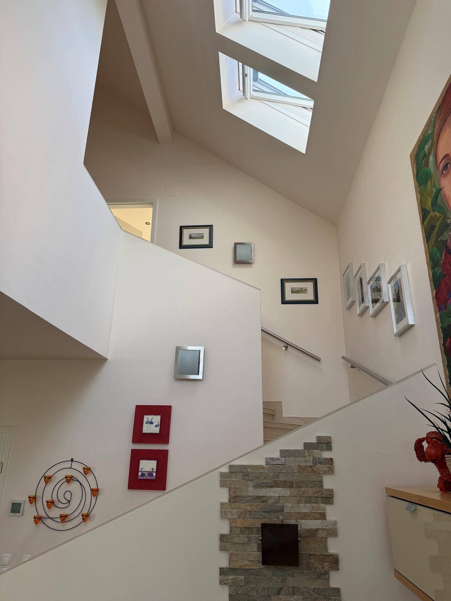 Offener Treppenbereich mit hohen Decken, Dachfenstern und dekorativen Steinakzenten an der Wand.