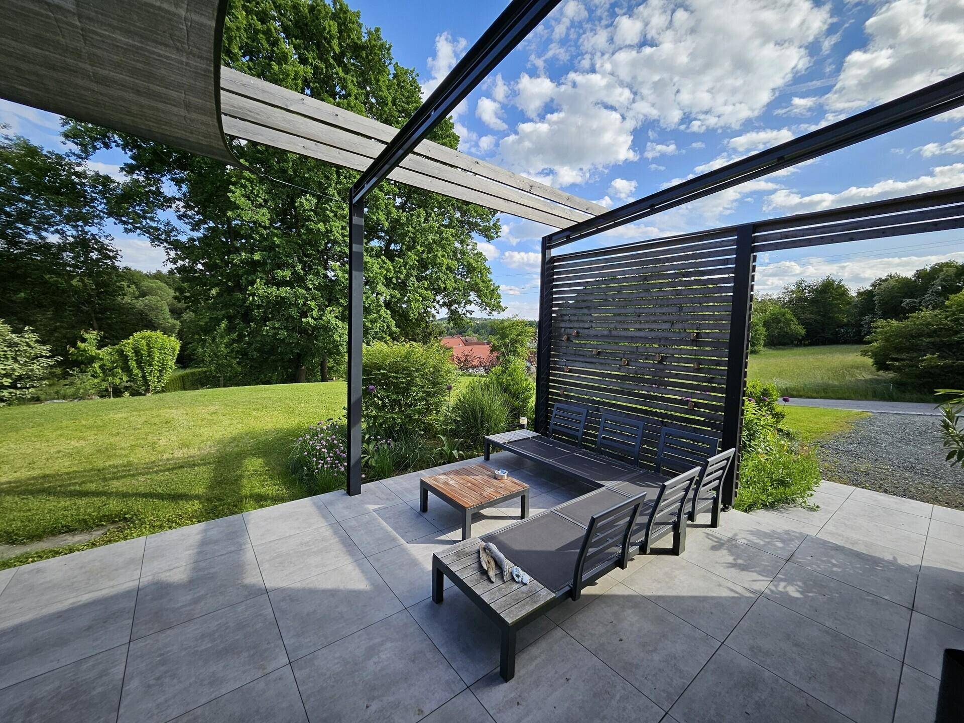 Geräumige Terrasse mit Lounge-Möbeln, Pergola und freiem Blick in die Natur.