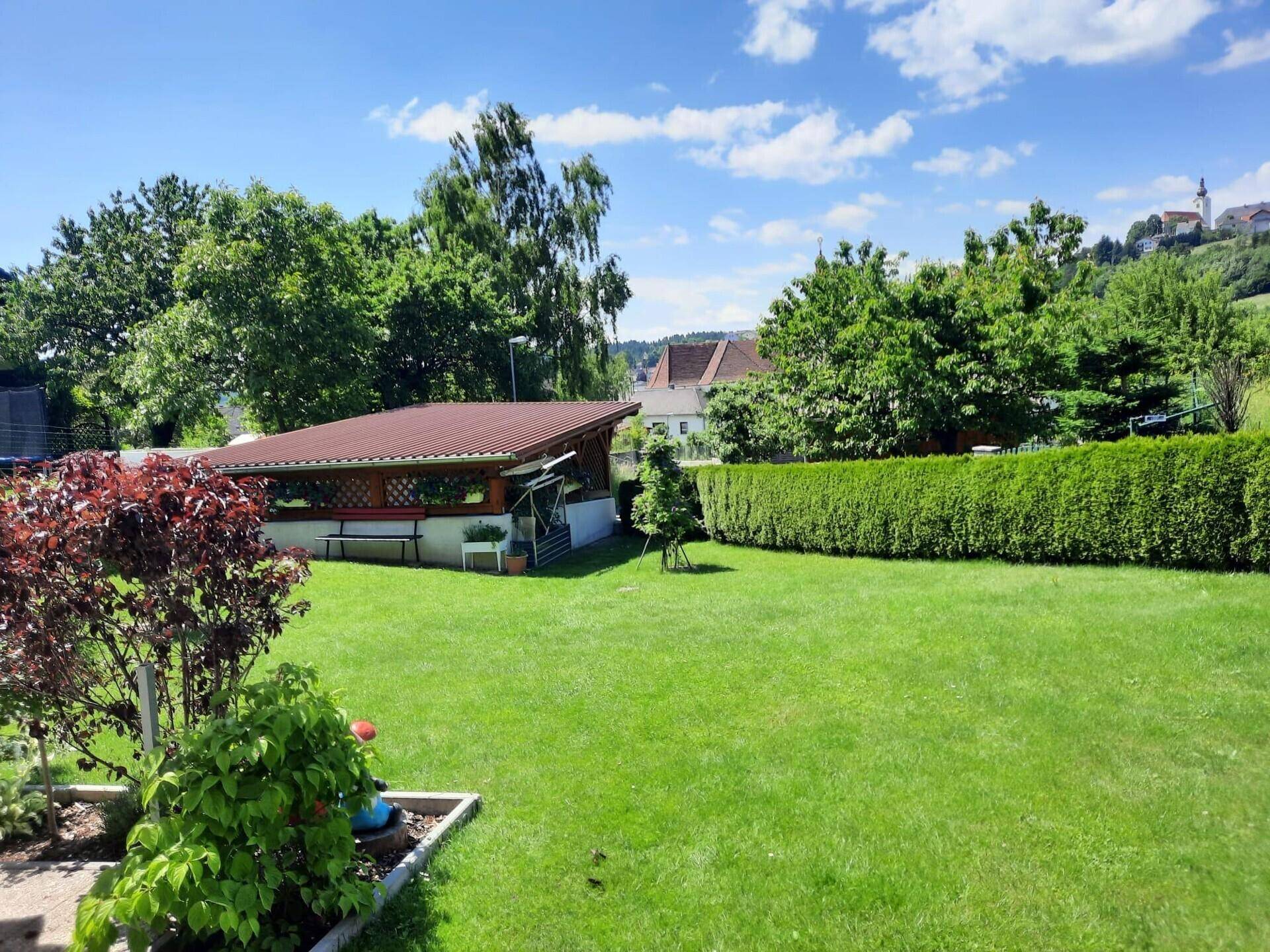 Großer, gepflegter Rasengarten mit Gartenhaus und Blick auf die umliegende Ortschaft.