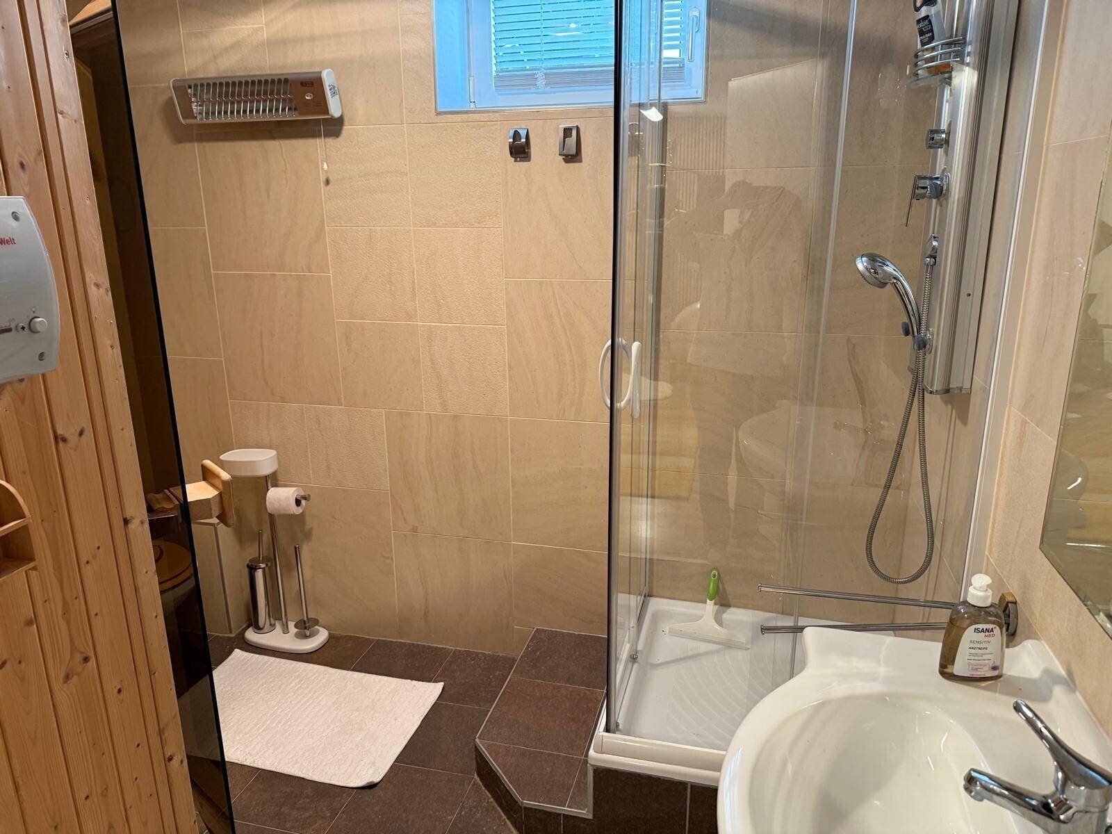 Badezimmer mit Dusche, Waschbecken und WC, direkt neben der Sauna gelegen für Wellness-Erlebnisse.