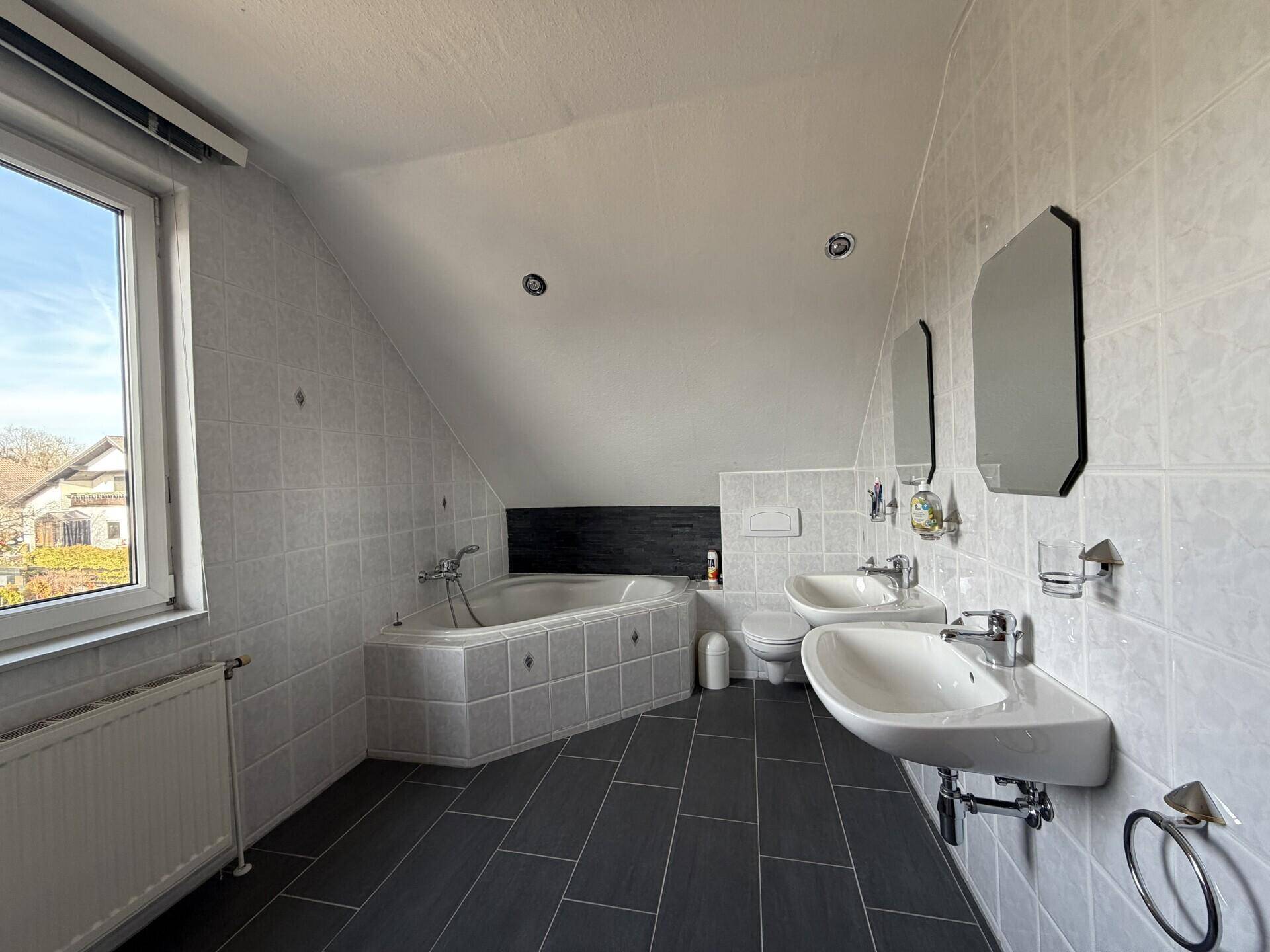 Helles Badezimmer im Dachgeschoss mit Badewanne, Doppelwaschbecken und Fenster.
