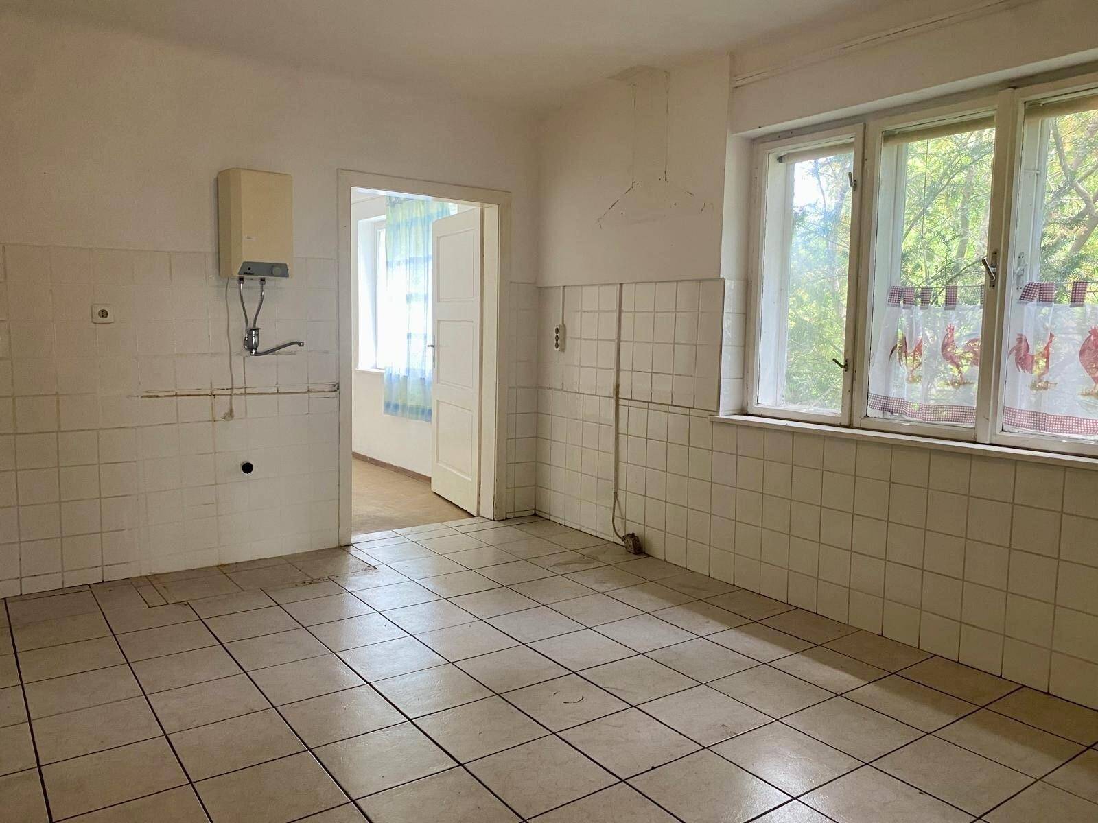 Leere Küche mit gefliesten Wänden, Fliesenboden und einem Fenster mit Blick ins Grüne.
