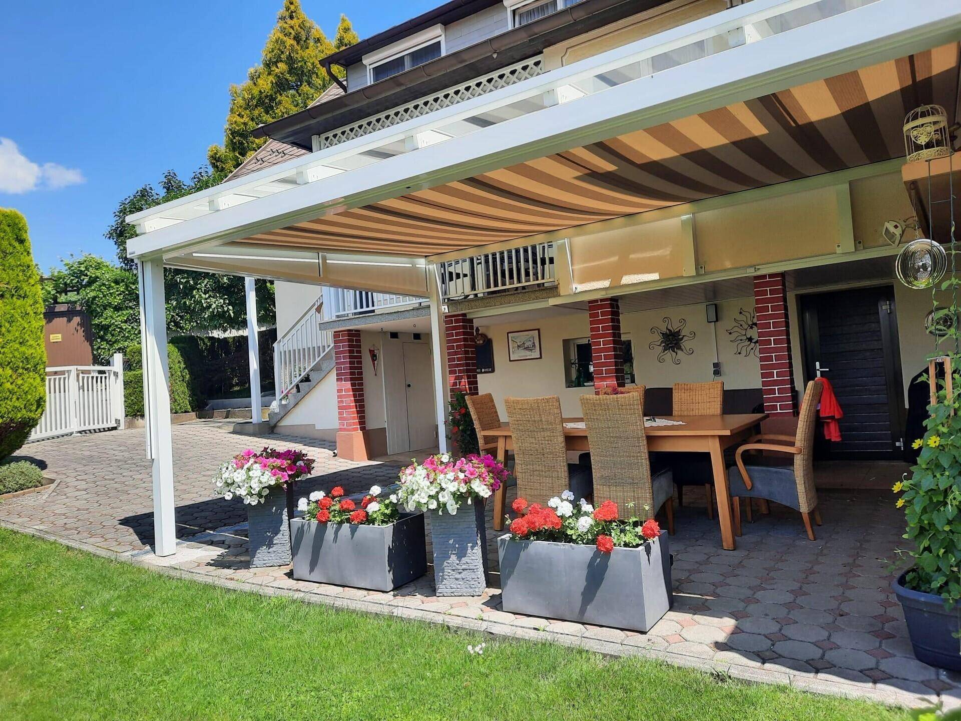 Überdachte Terrasse mit Esstisch und bunten Blumen, ideal für Mahlzeiten im Freien.