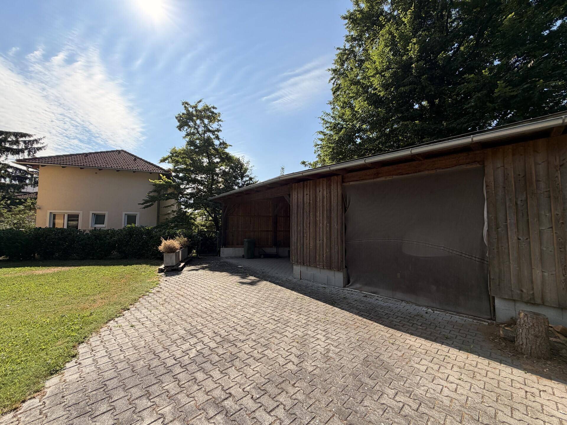 Gepflasterte Auffahrt führt zu einem Holzschuppen oder einer Garage, umgeben von Grün.
