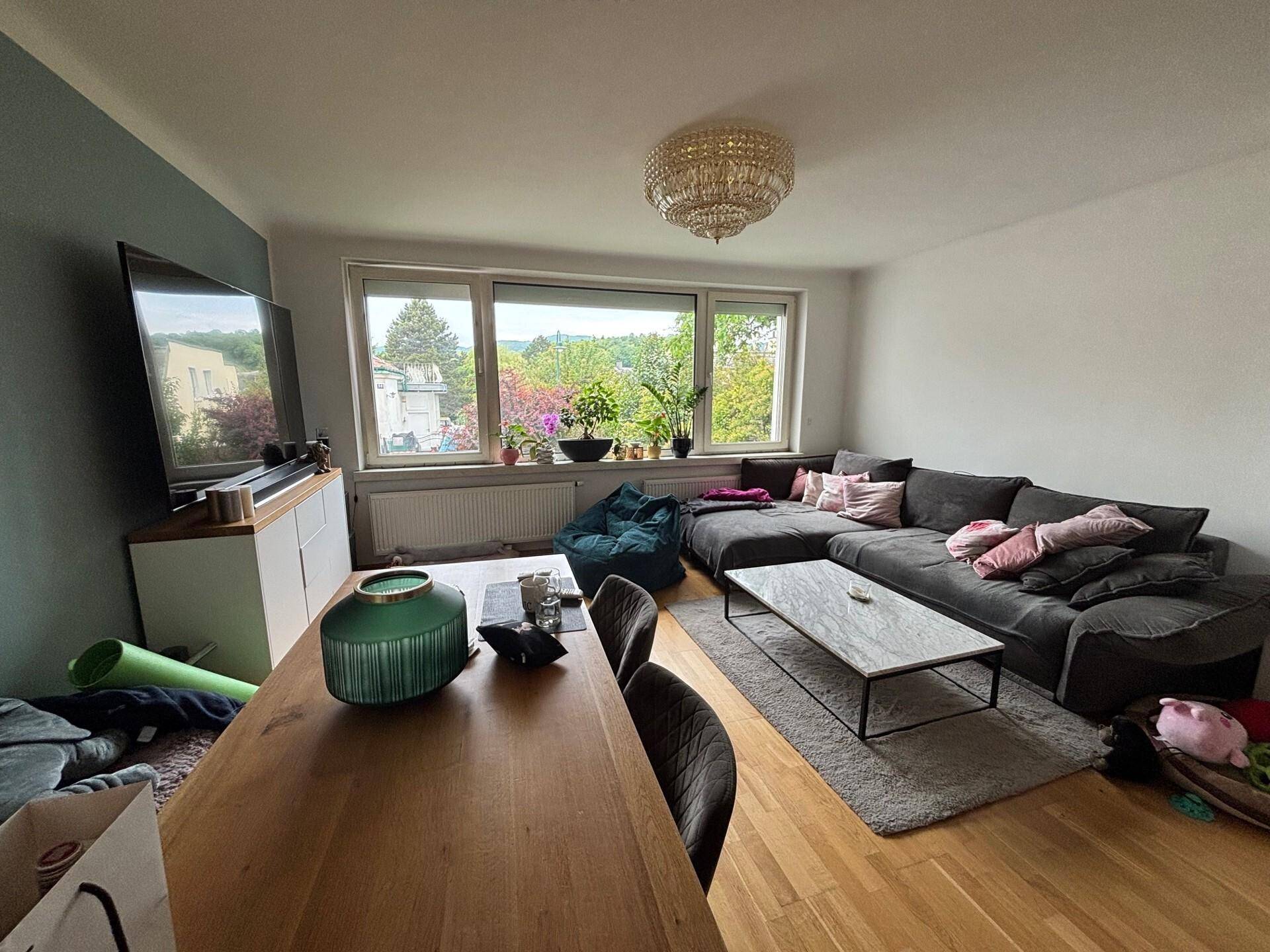 Heller Wohn-Essbereich mit Holzboden, großem Sofa und Esstisch sowie weitem Ausblick ins Grüne.