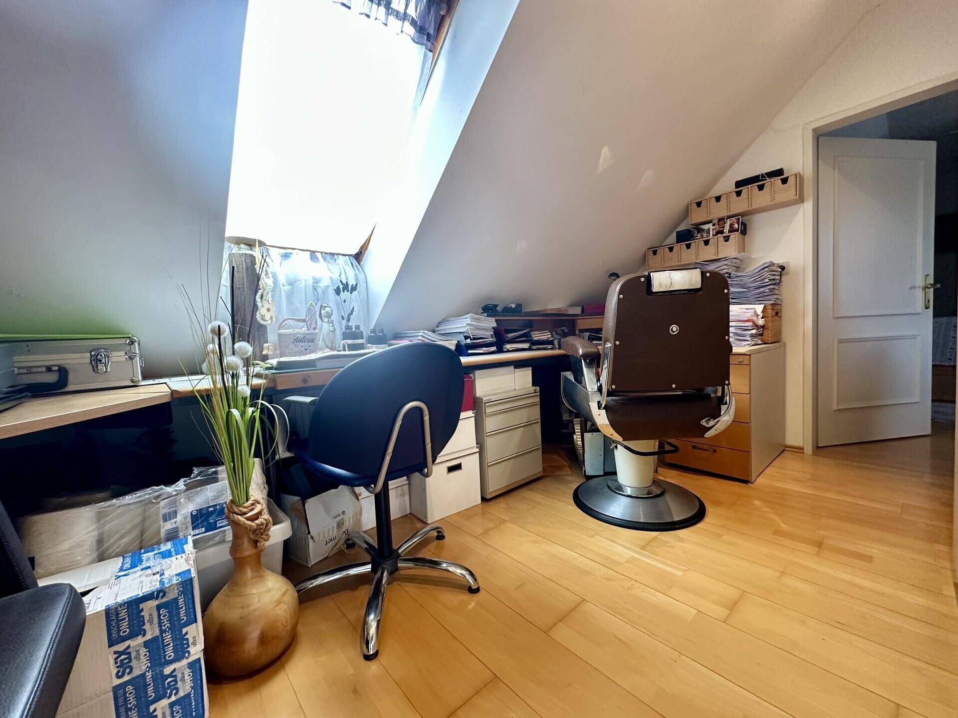 Büro im Dachgeschoss mit schrägen Wänden, Holzfußboden und einem Schreibtisch.