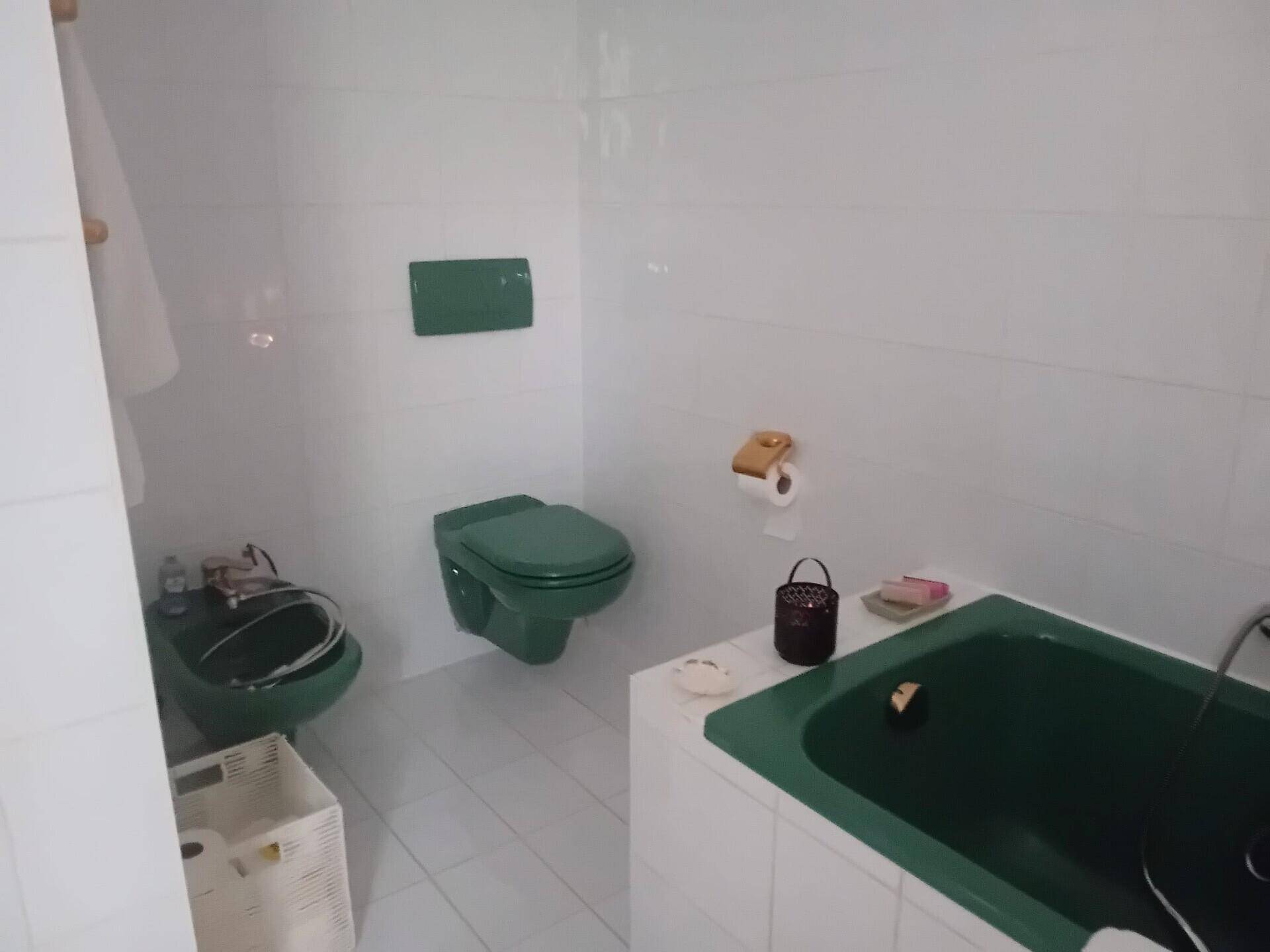 Badezimmer mit grüner Badewanne, Toilette und Bidet, weißen Fliesen.