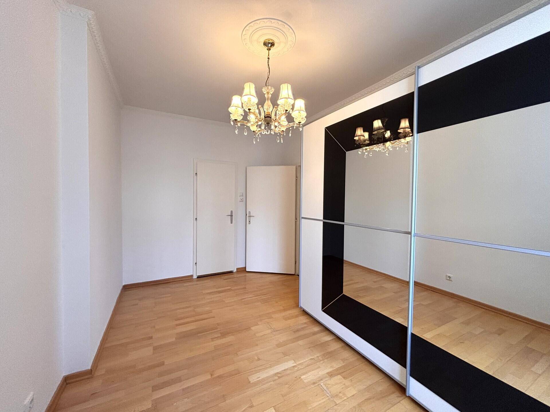 Schlafzimmer mit Spiegelschrank, Holzboden und zwei Türen, die zu anderen Räumen führen.