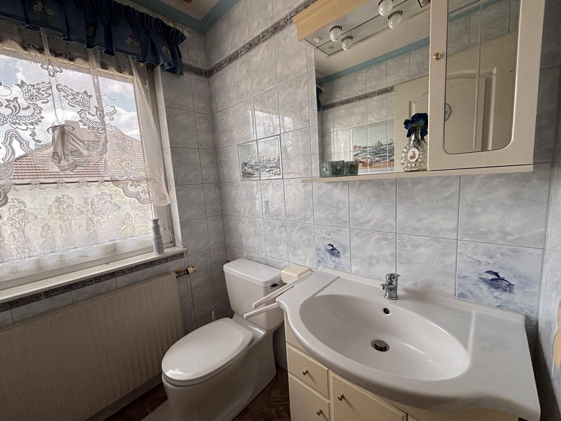Kleines Badezimmer mit WC, Waschbecken und Fenster, ausgestattet mit blauen Fliesen.