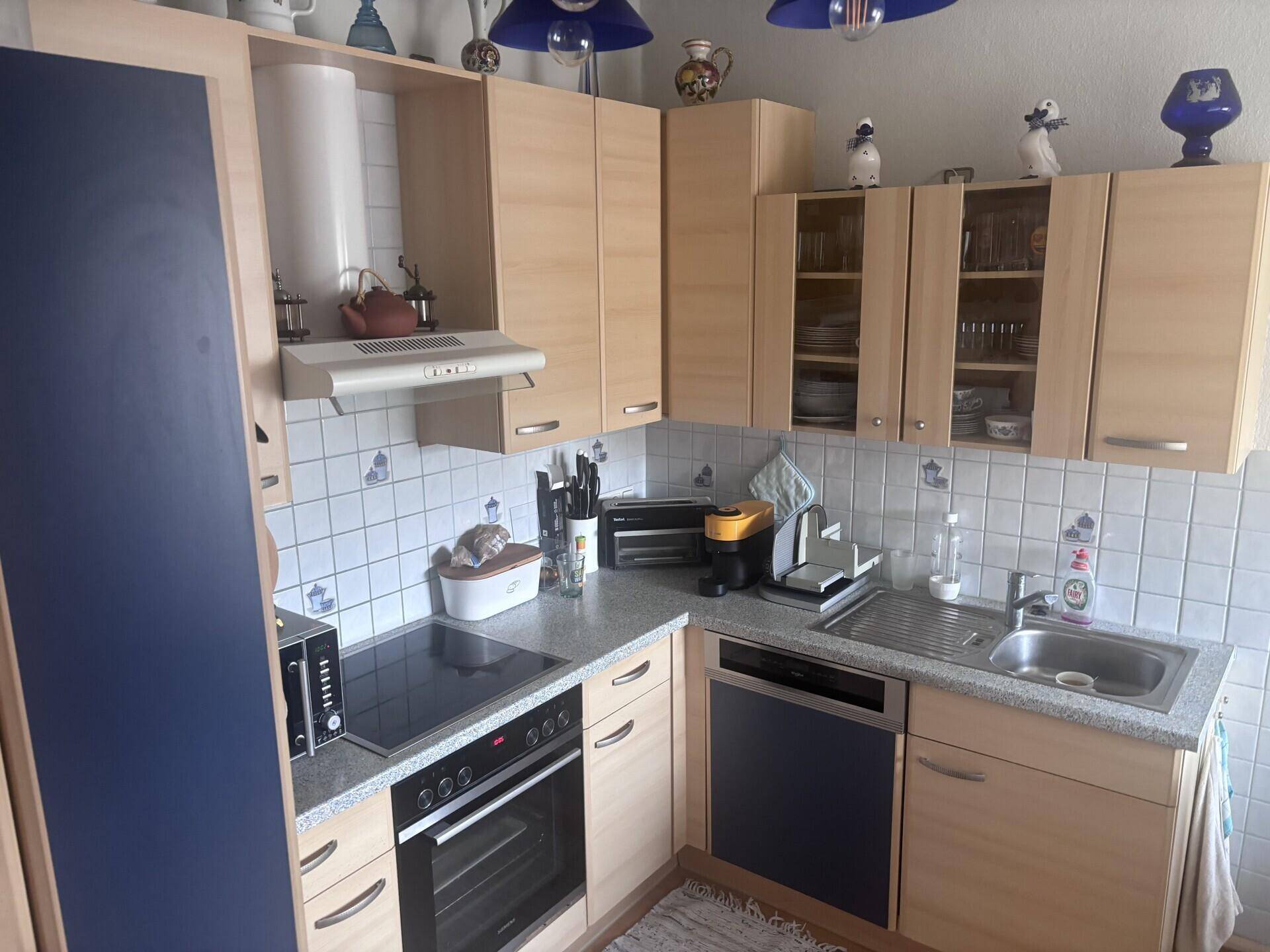 Funktionale Küche mit hellen Holzschränken, blauen Akzenten und integrierten Geräten.
