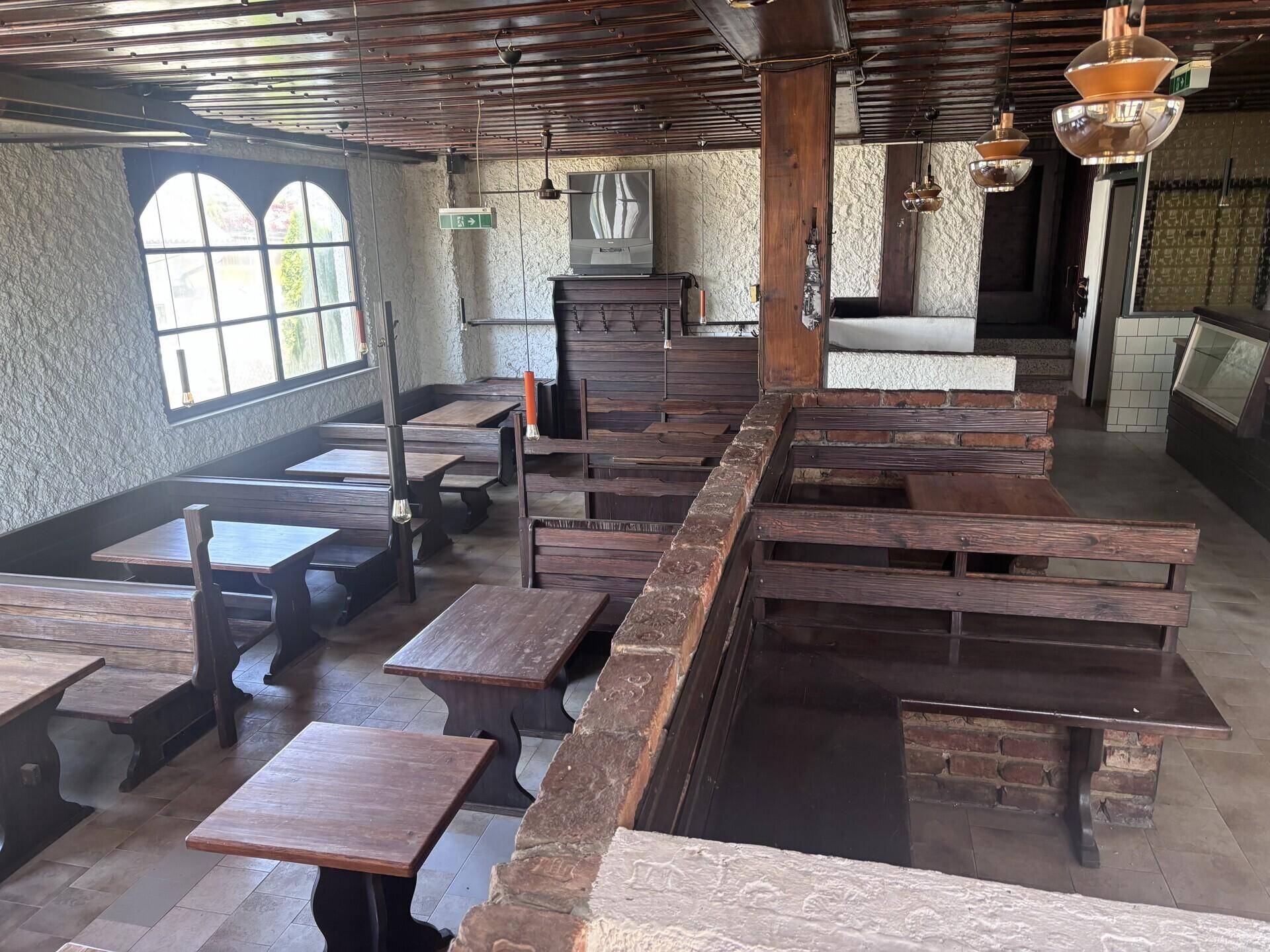 Rustikaler Gastraum mit Holztischen und -bänken, strukturierten Wänden und großen Fenstern.