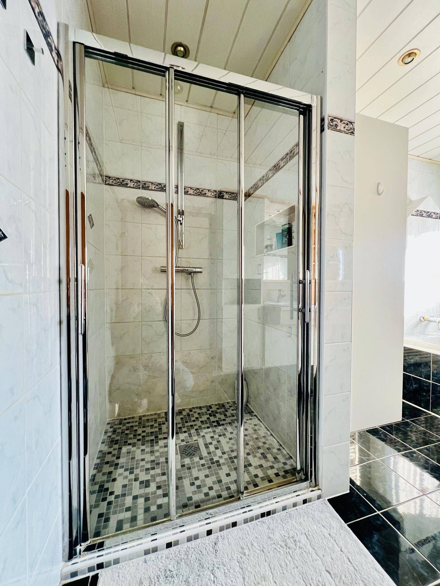Duschkabine mit Glaswänden und Mosaikfliesen im Badezimmer.