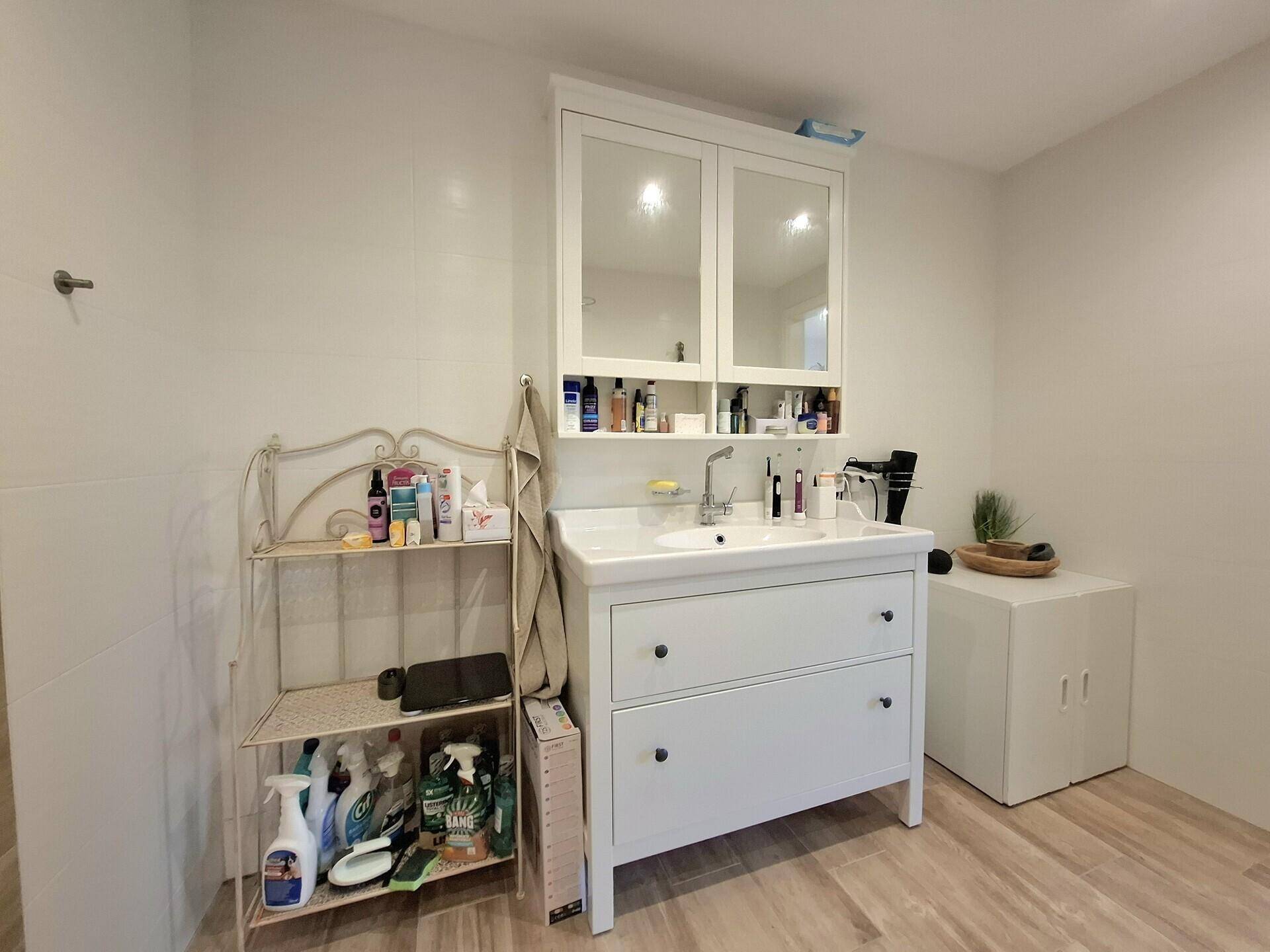 Helles Badezimmer mit Einzelwaschbecken, Spiegelschrank und Holzoptik-Fliesenboden.