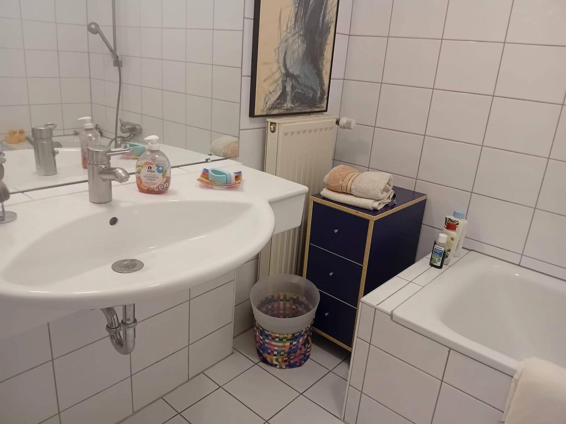 Badezimmer mit Waschbecken, Badewanne und weißen Fliesen, Spiegel und Heizkörper.