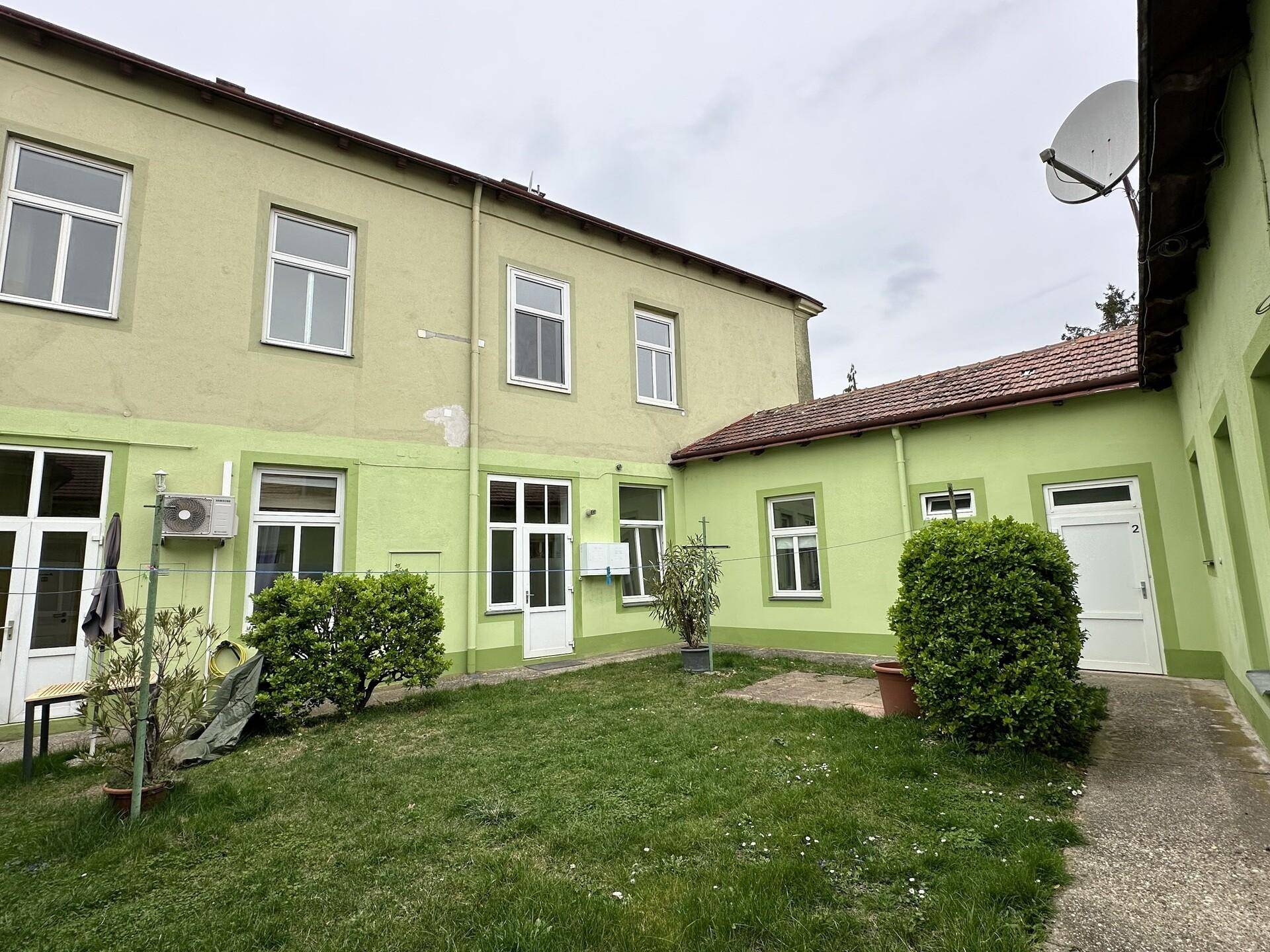 Grüner Hinterhof mit Rasen und Zugangstüren zu den Wohneinheiten.