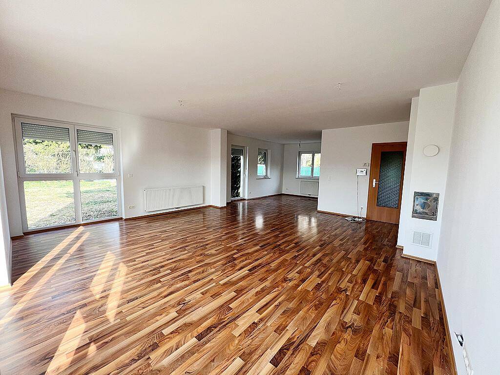 Geräumiges, helles Wohnzimmer mit Laminatboden, großen Fenstern und Zugang zum Garten.