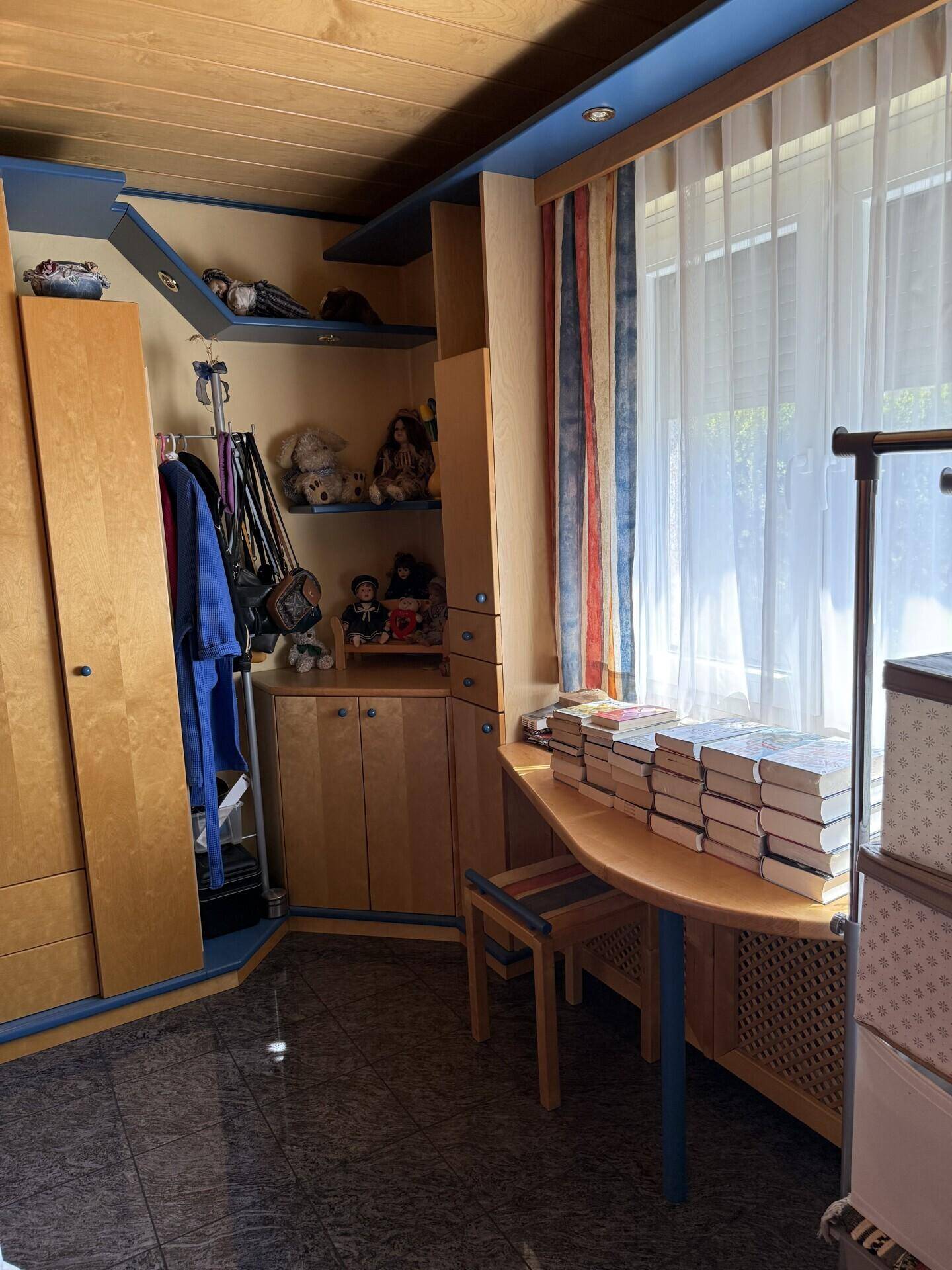 Kinderzimmer mit Holzmöbeln, Einbauschränken und Fenster mit bunten Vorhängen.
