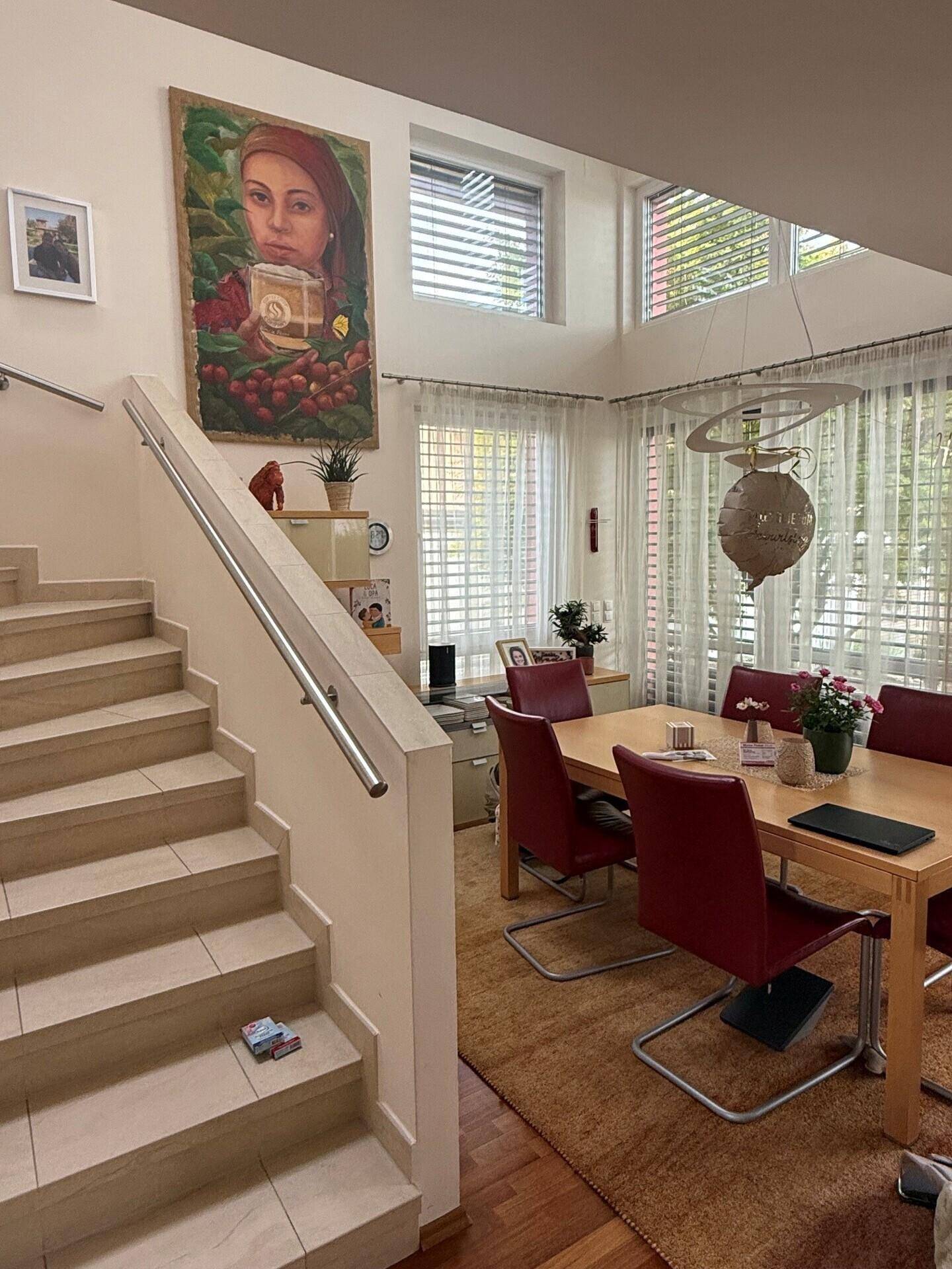 Heller Essbereich mit Holztisch, roten Stühlen, hohen Decken und einer modernen Treppe.