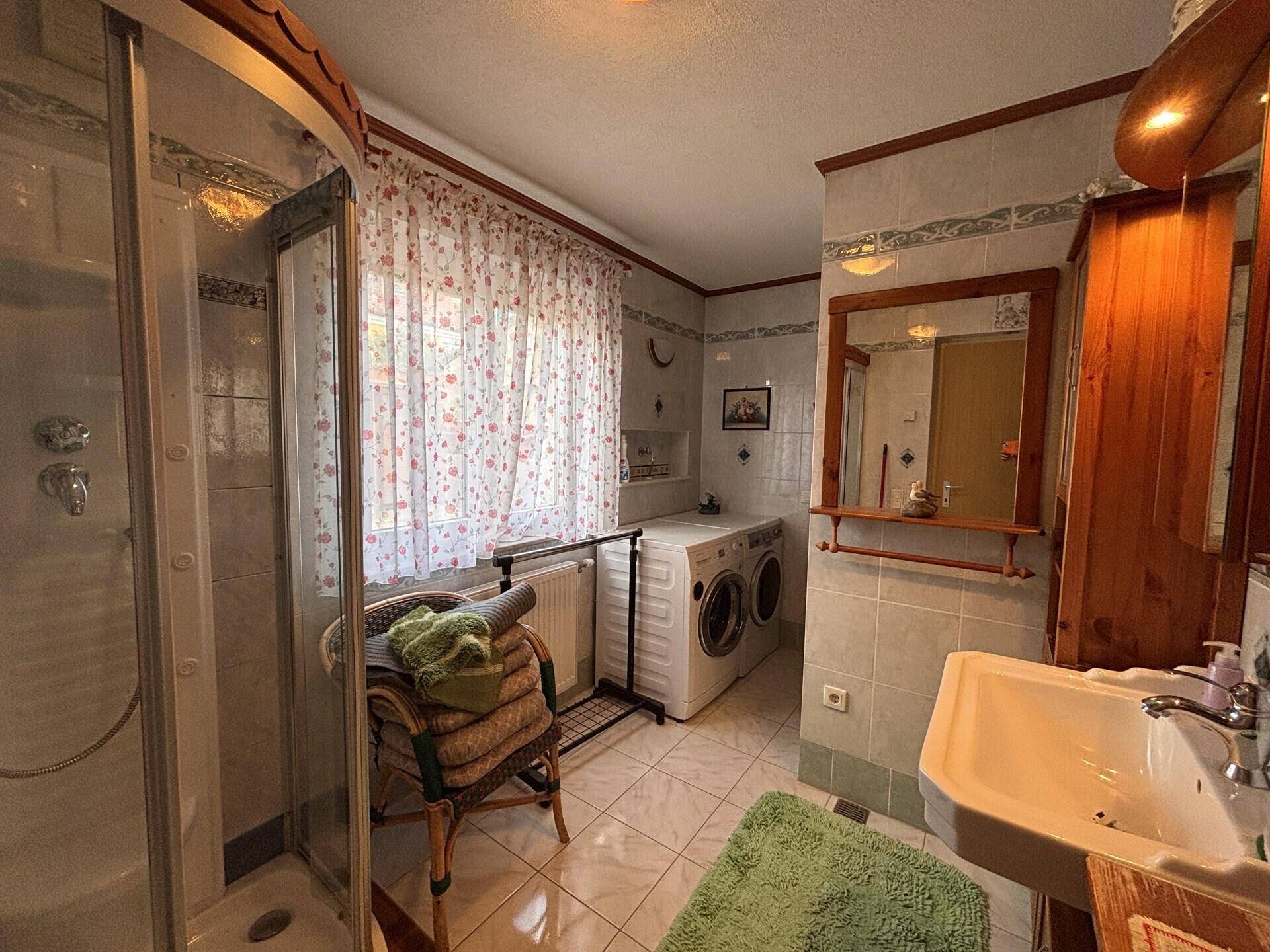 Badezimmer mit Duschkabine, Waschmaschine, Trockner und einem einzelnen Waschbecken.