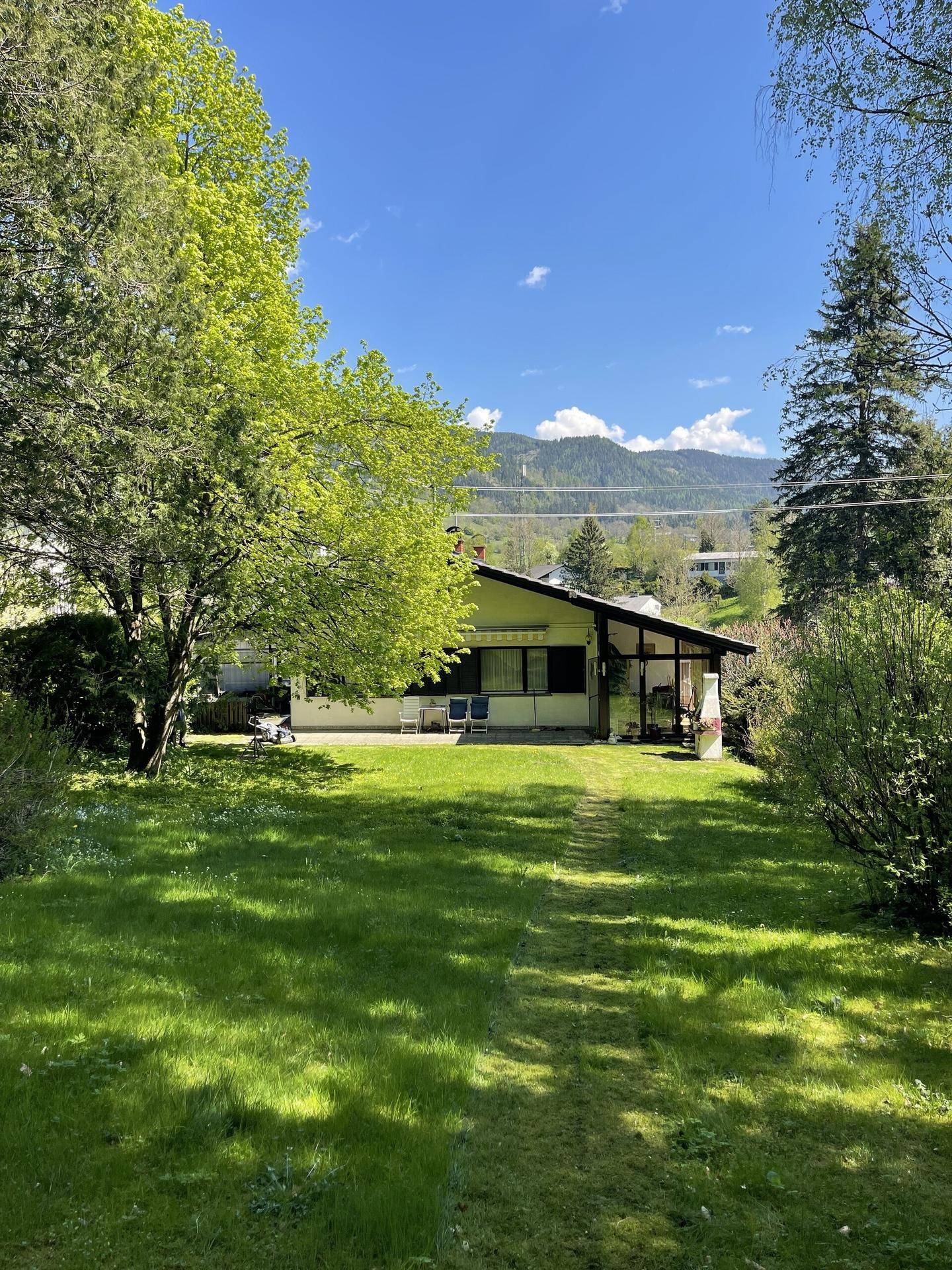 Großer grüner Garten mit Rasenfläche, Bäumen und Blick auf die Berge im Hintergrund.
