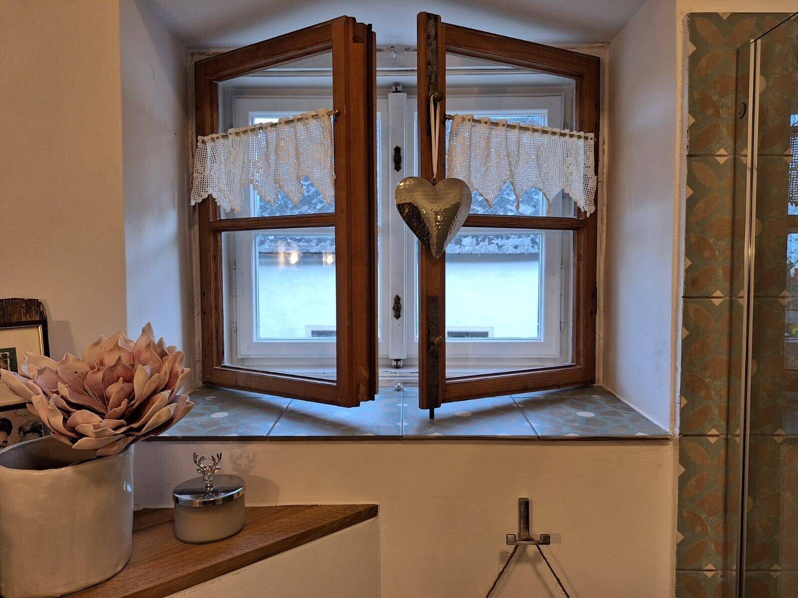 Kleines Badezimmerfenster mit Spitzenvorhängen und traditioneller Dekoration.
