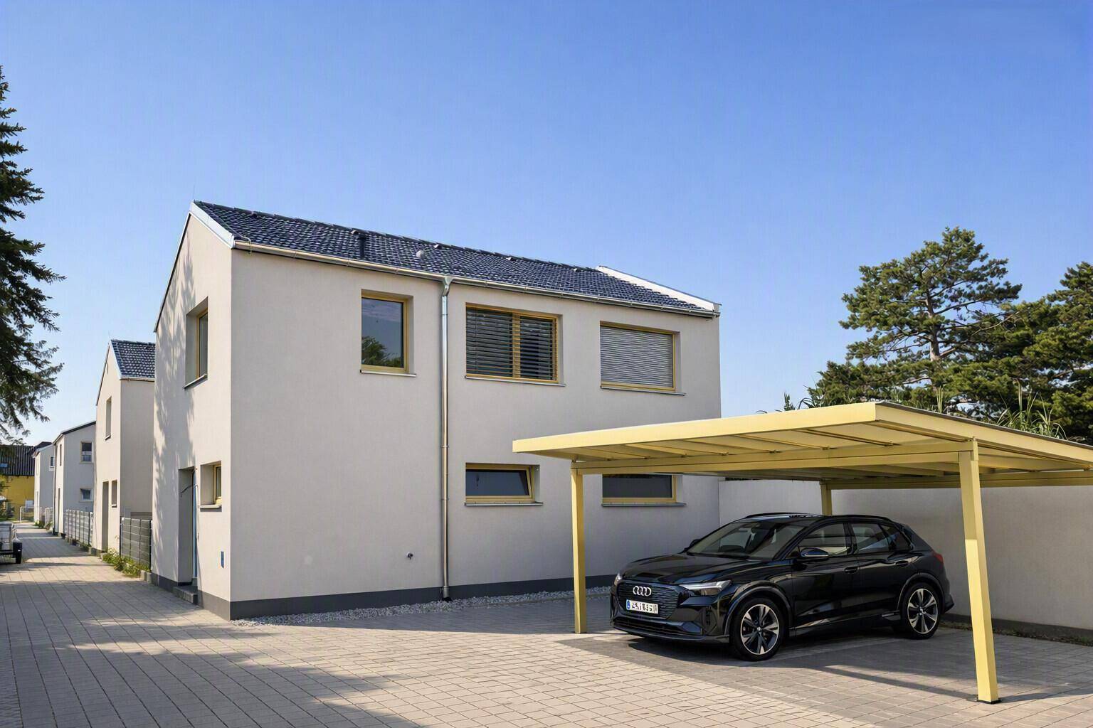 Modernes Einfamilienhaus mit Carport, gepflasterter Auffahrt und einem Auto.