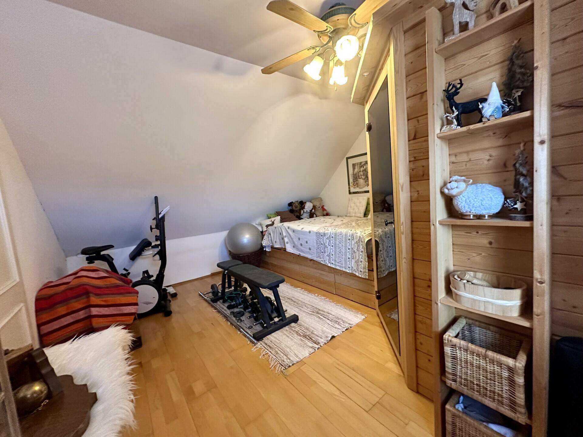 Schlafzimmer mit Holzboden, Sauna und Fitnessgeräten unter der Dachschräge.