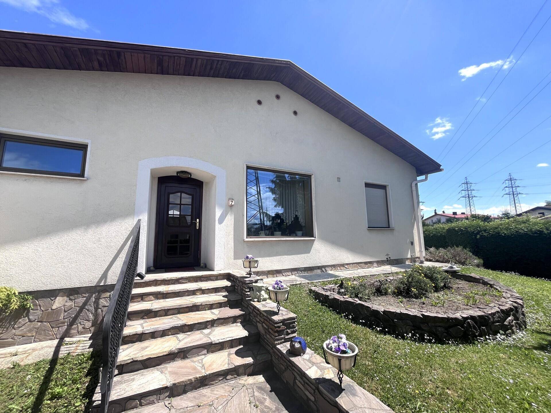 Eingangsbereich des Hauses mit Steintreppe, gepflegtem Vorgarten und sonnigem Wetter.