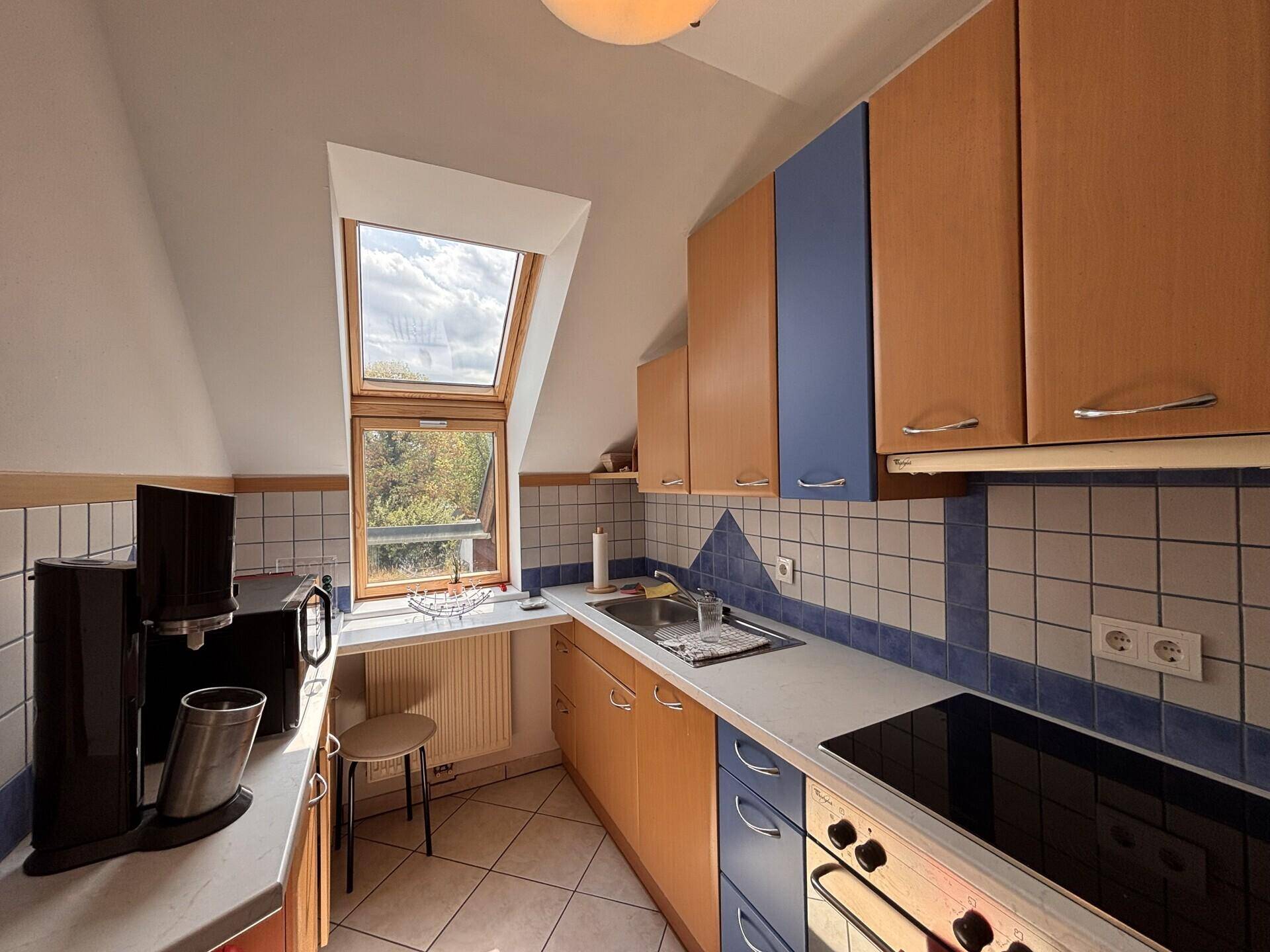 Küche mit Holz- und blauen Schränken, Dachfenster und gefliestem Spritzschutz.