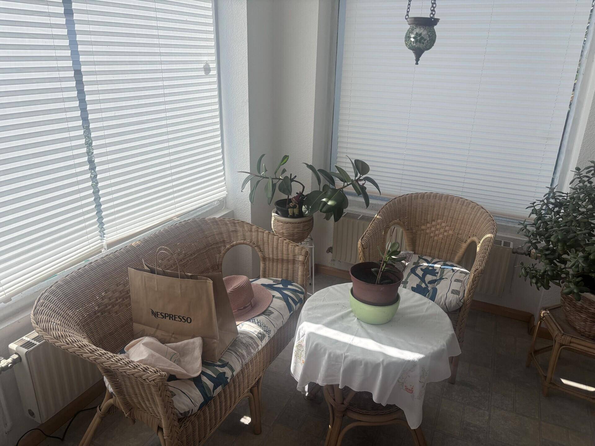 Heller Wintergarten mit Korbmöbeln und vielen Pflanzen, ideal zum Entspannen und Sonnenbaden.