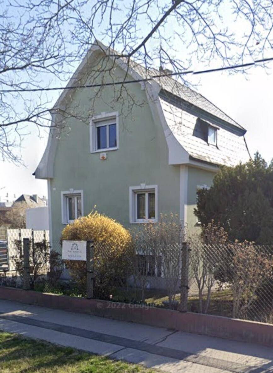 Vorderansicht eines charmanten Hauses mit hellgrüner Fassade und Mansarddach, umgeben von einem kleinen Vorgarten.