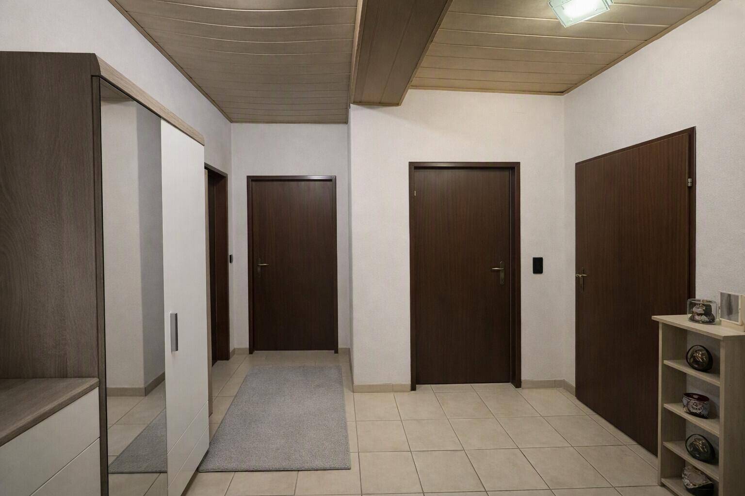 Heller Flur mit Fliesenboden, dunklen Türen und einem Spiegelschrank.