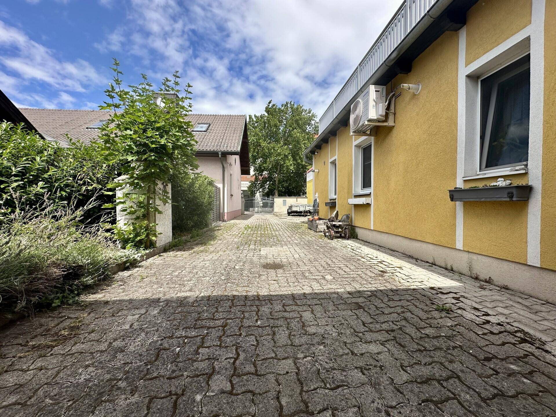 Gepflasterte Einfahrt neben einem gelben Gebäude unter blauem Himmel.