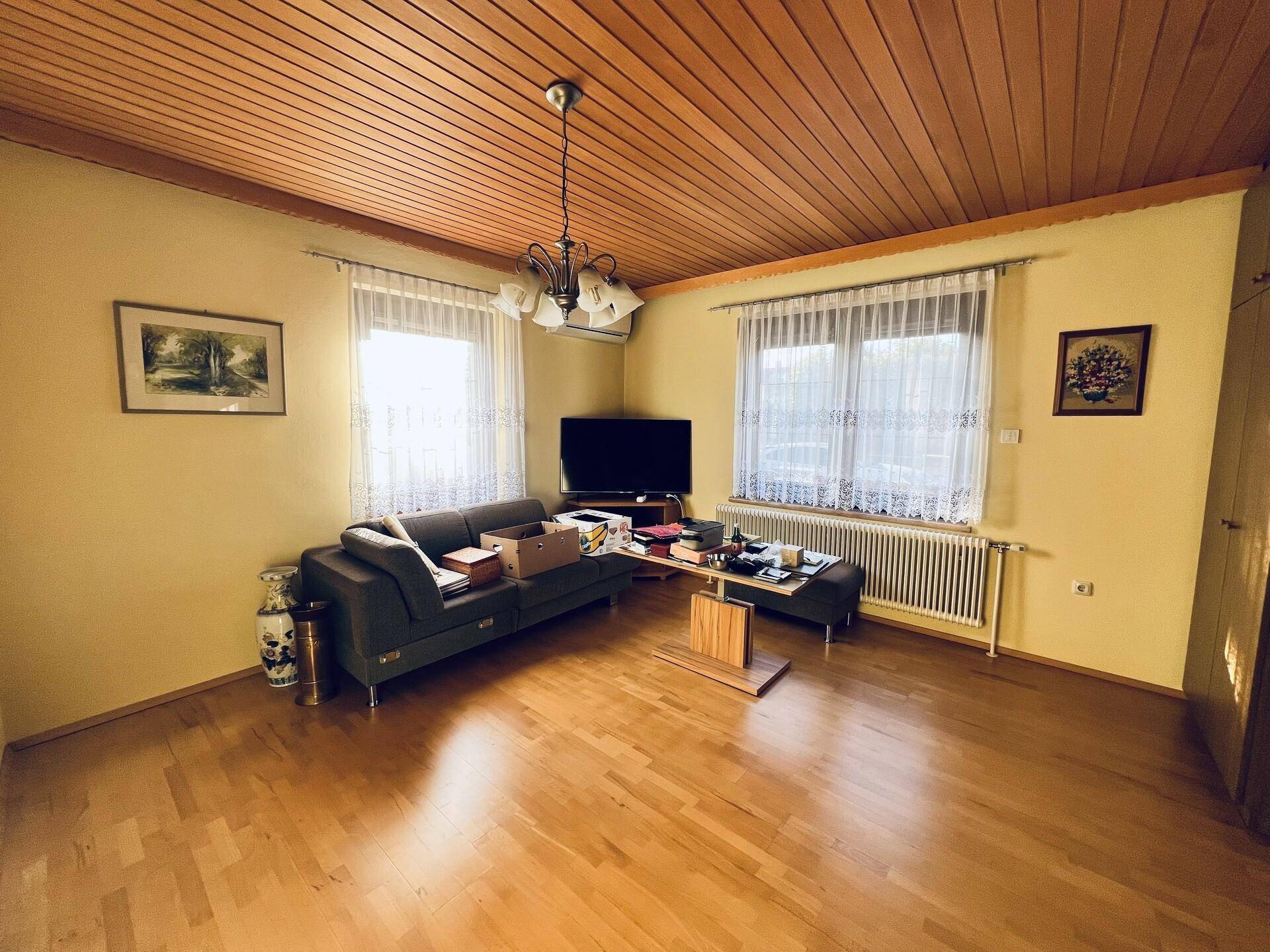 Helles Wohnzimmer mit Holzbalkendecke, Parkettboden und gemütlichem Sofa, gut gepflegt.