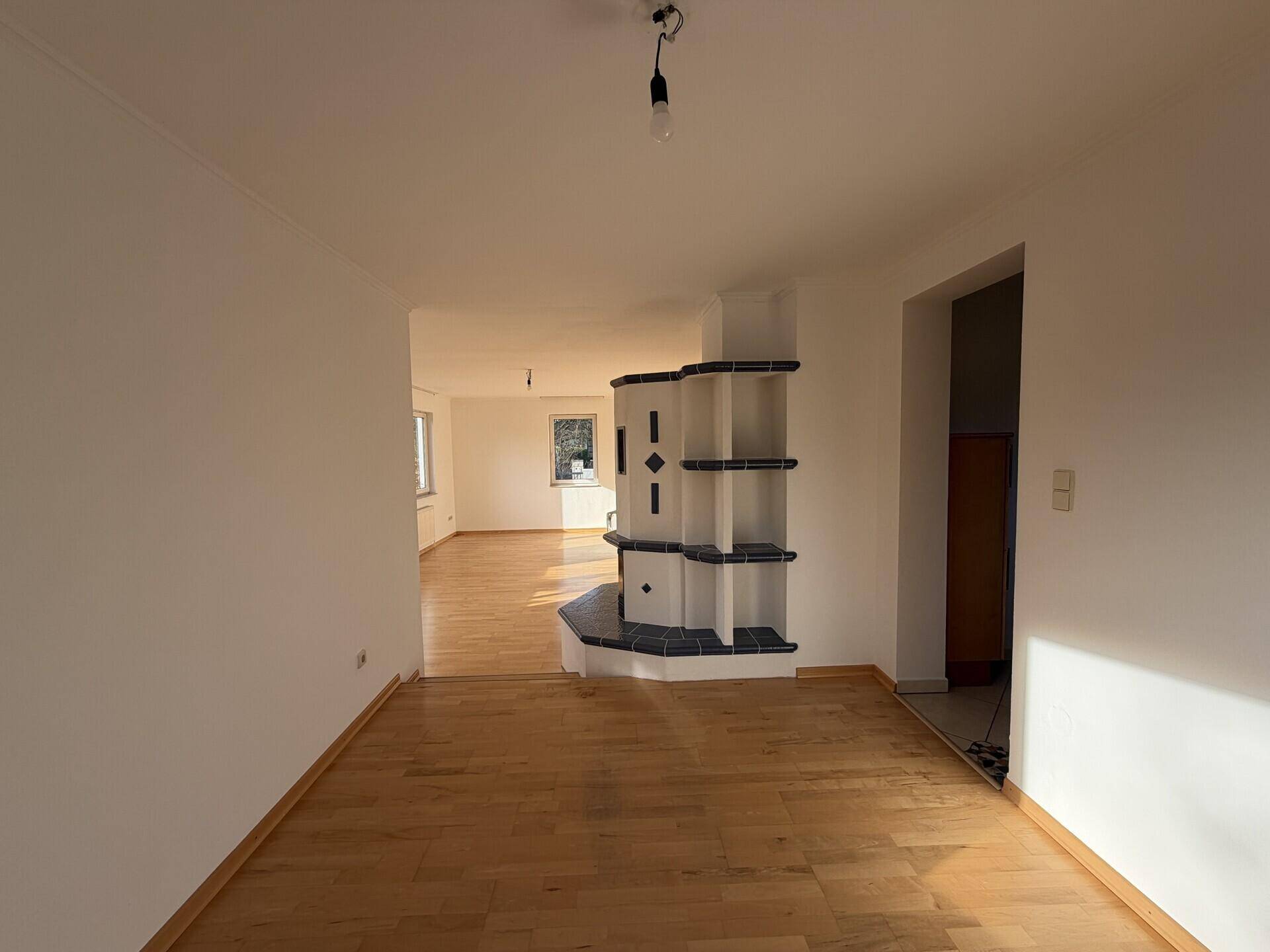 Geräumiger Wohnbereich mit Parkettboden und einem dekorativen Kachelofen als Blickfang.