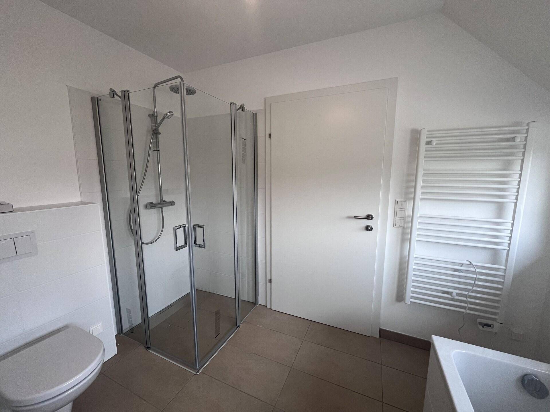 Modernes Badezimmer mit Duschkabine, WC und beheiztem Handtuchhalter.